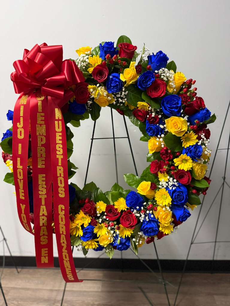 Circular floral wreath with red, blue, and yellow roses and a large red bow