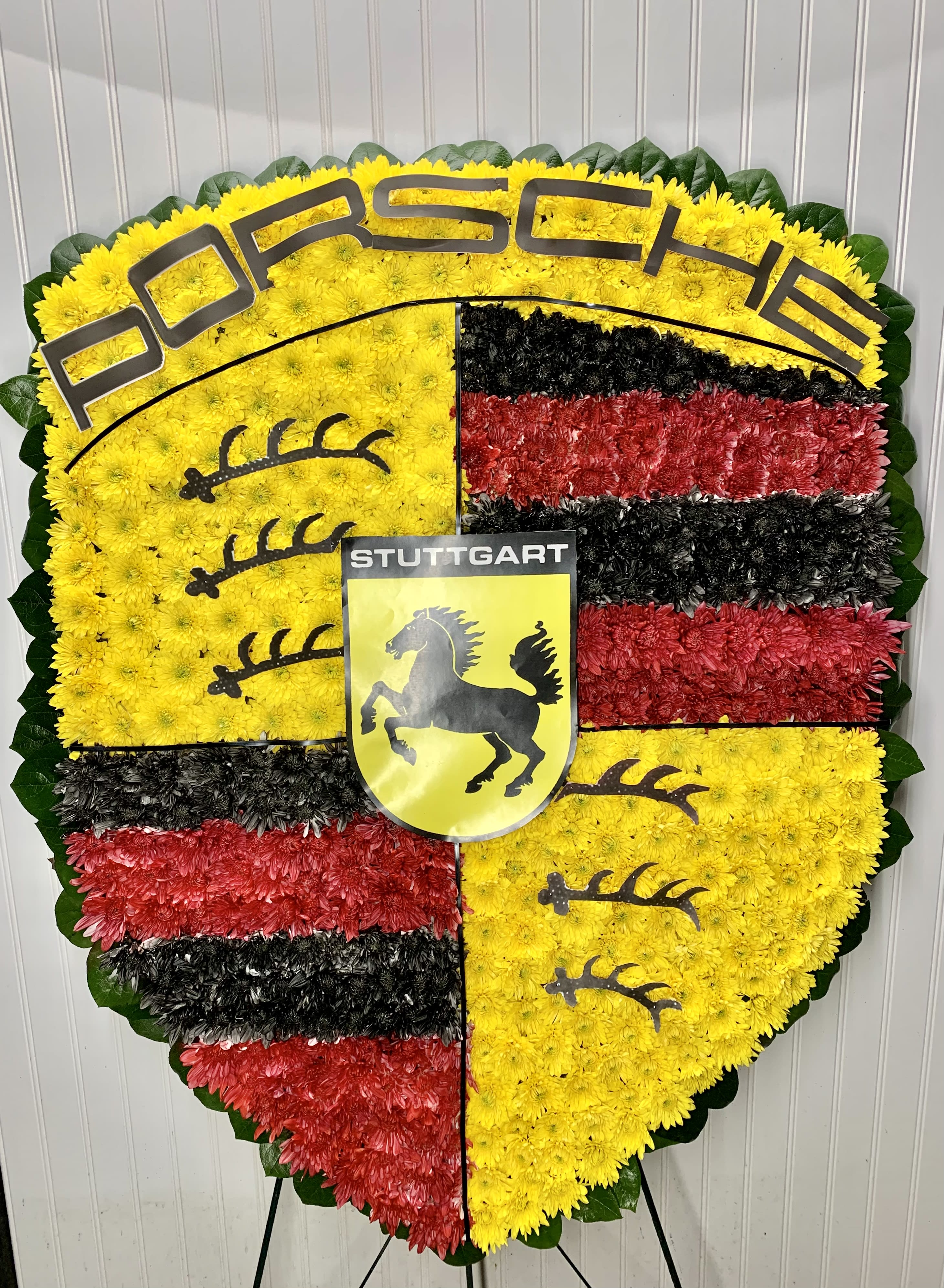 Heart-shaped floral tribute in yellow, red, and black with Porsche and Stuttgart emblems