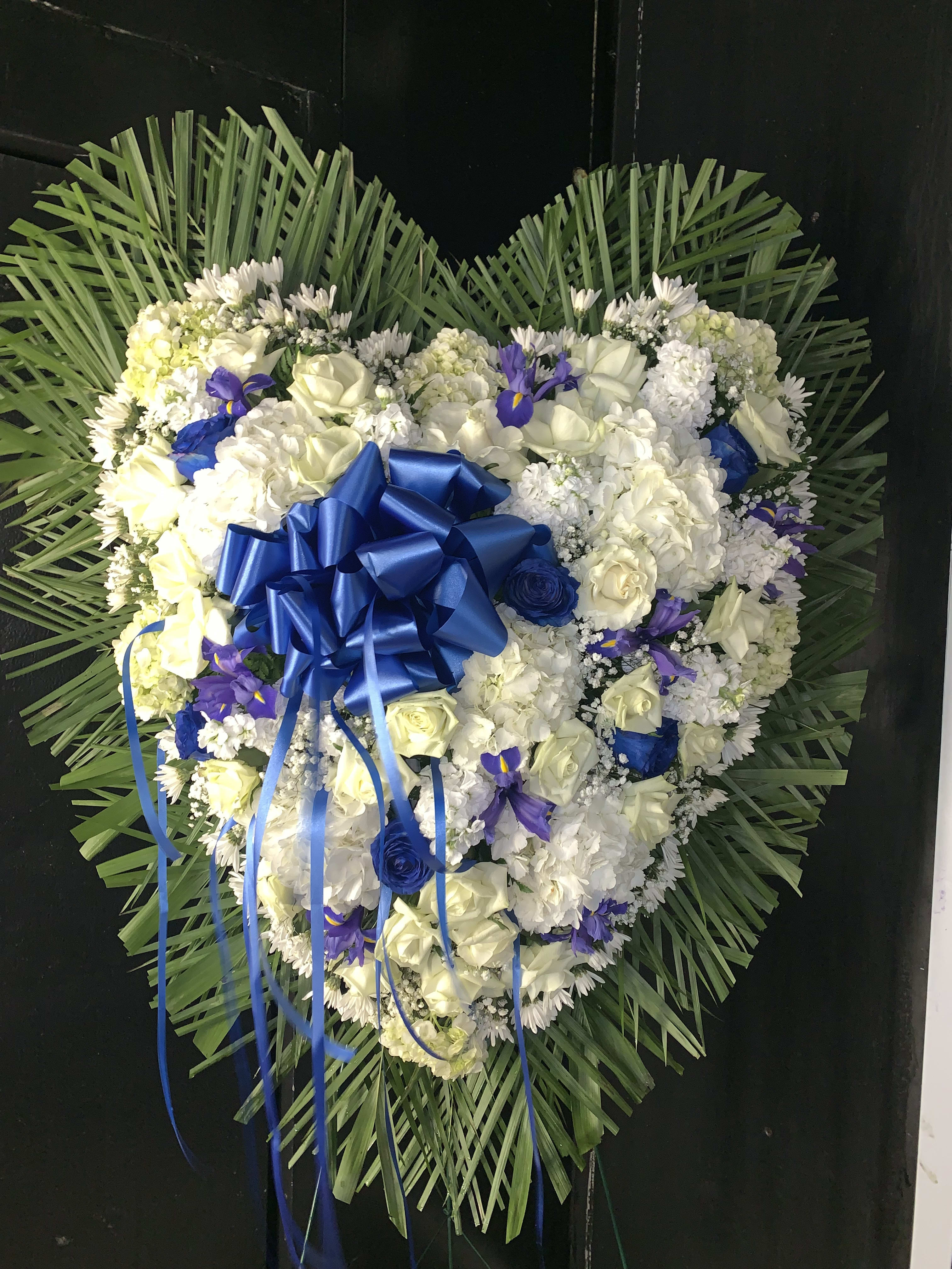 Heart-shaped floral wreath with white and blue flowers and a blue ribbon bow