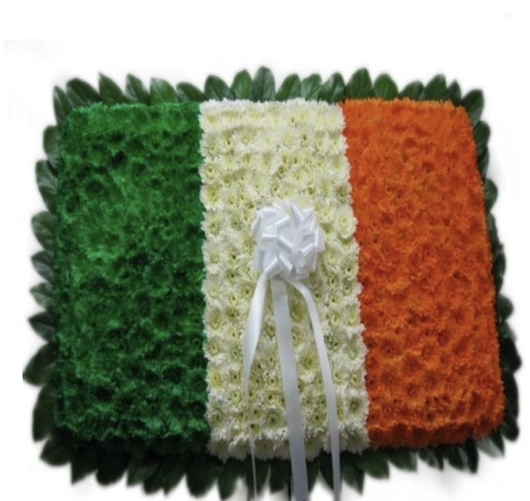 Floral tribute in green, white, and orange with a white ribbon bow