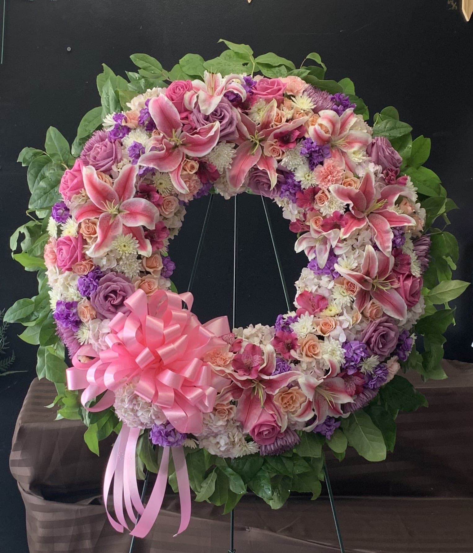 Heart-shaped floral wreath with pink lilies, roses, and a pink ribbon bow