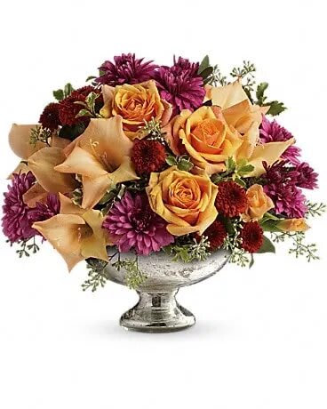 Low centerpiece of orange roses, peach calla lilies, and purple mums in a silver pedestal bowl