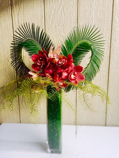 Red orchid arrangement in a tall green vase with palm fronds
