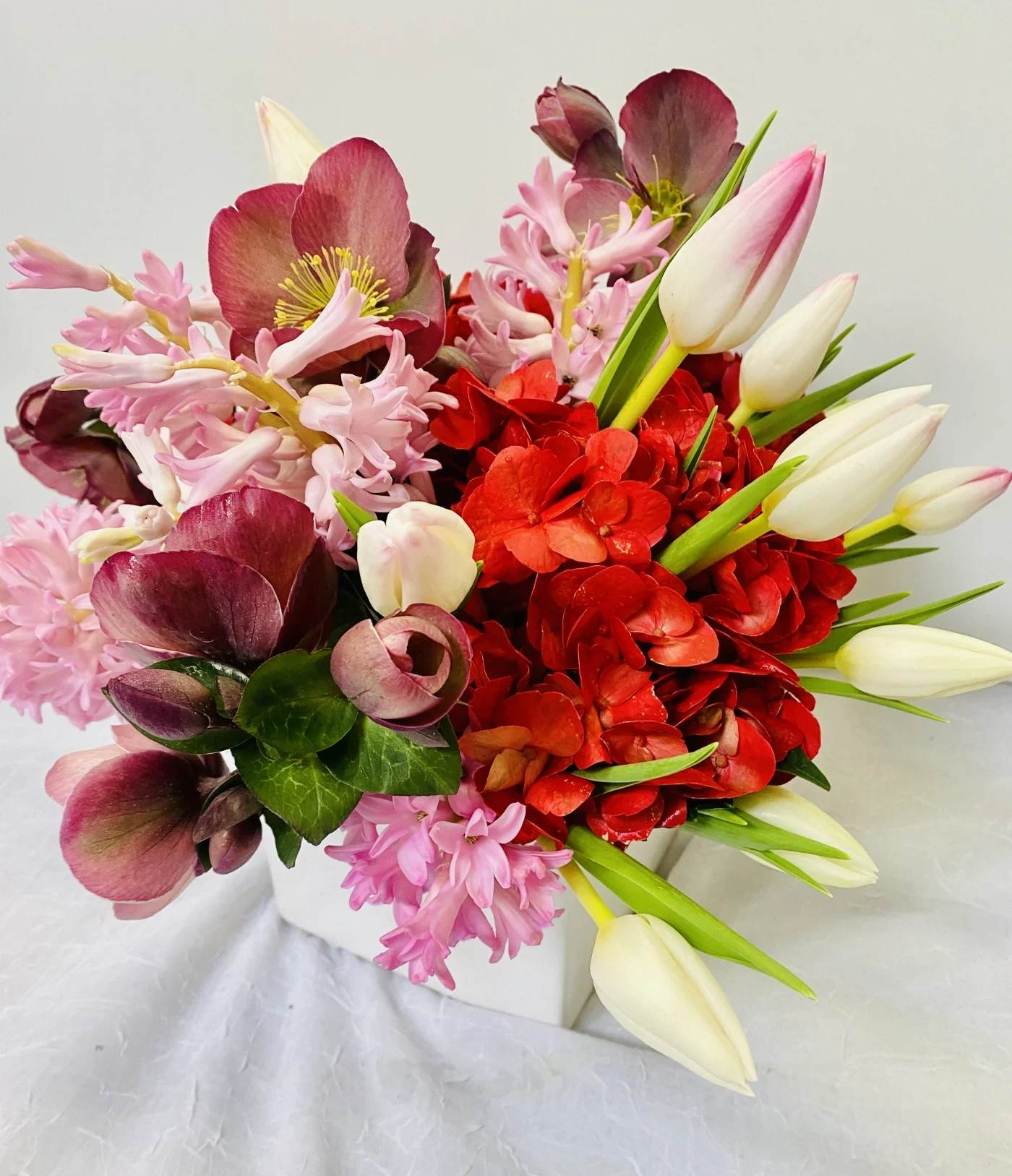 Bouquet of red and pink flowers with white tulip buds in a white container