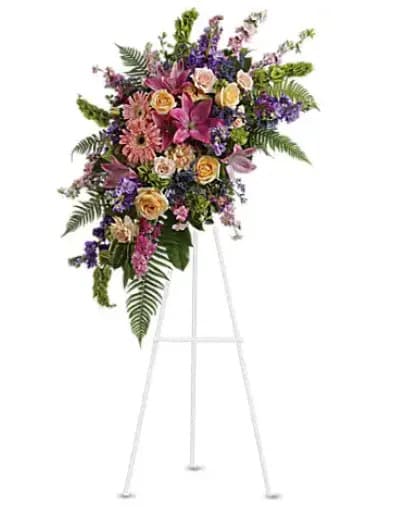 Heavenly Grace Spray - A sublime garden of rich yet subtle hues is a touching tribute to a lifetime of memories and special moments as varied and dear as this palette of blooms. A lovely assortment of flowers such as pink roses, larkspur, asiatic lilies, gerberas and sinuata statice, with peach roses and carnations, purple stock and limonium, and bells of Ireland on a classic easel. 