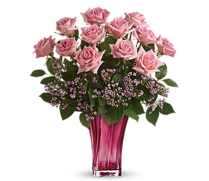 Pink roses arranged in a tall glass vase with small purple filler flowers