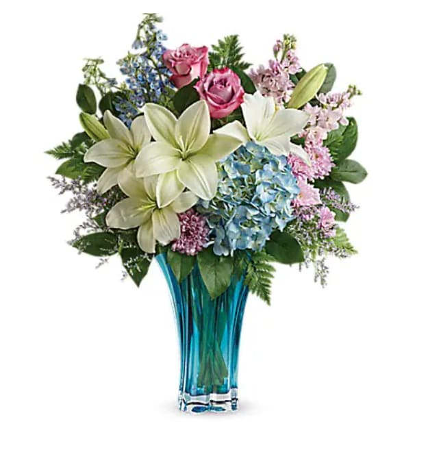 Bouquet of lilies, roses, hydrangeas, and mixed blooms in a blue glass vase