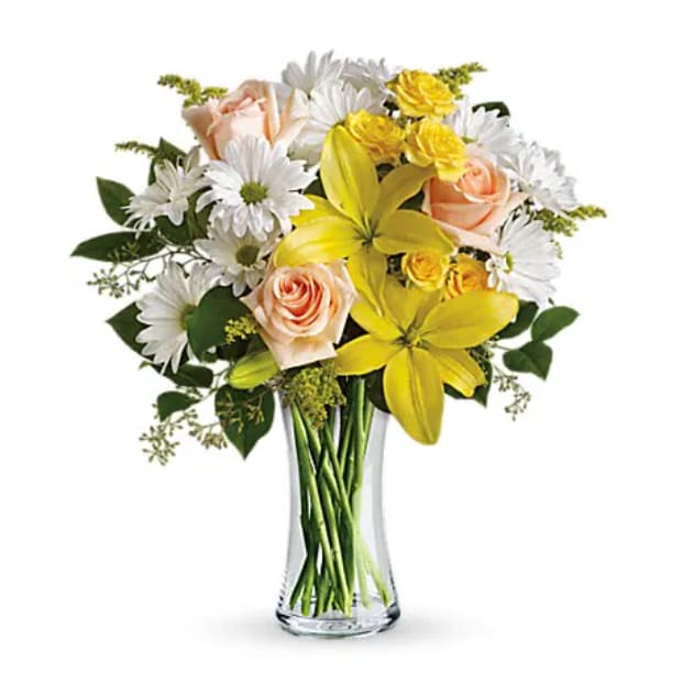 Bouquet of yellow lilies, peach roses, and white daisies in a clear glass vase