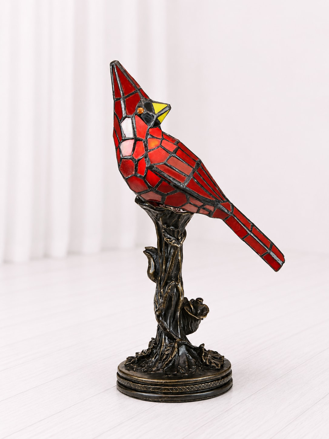 Cardinal Memorial Lamp - A beautiful symbol of love, remembrance, and comfort, this stained glass cardinal lamp brings warmth and meaning to any space. Designed with rich crimson red glass and detailed black metalwork, this elegant bird rests atop an ornate bronze-style base for a timeless look. Often seen as a sign from heaven, cardinals are a meaningful sympathy gift for those grieving the loss of a loved one. Perfect for memorial displays, cozy reading spaces, or everyday home décor, this lamp creates a soft and comforting glow when illuminated. Lamp is 13.5 inches tall.