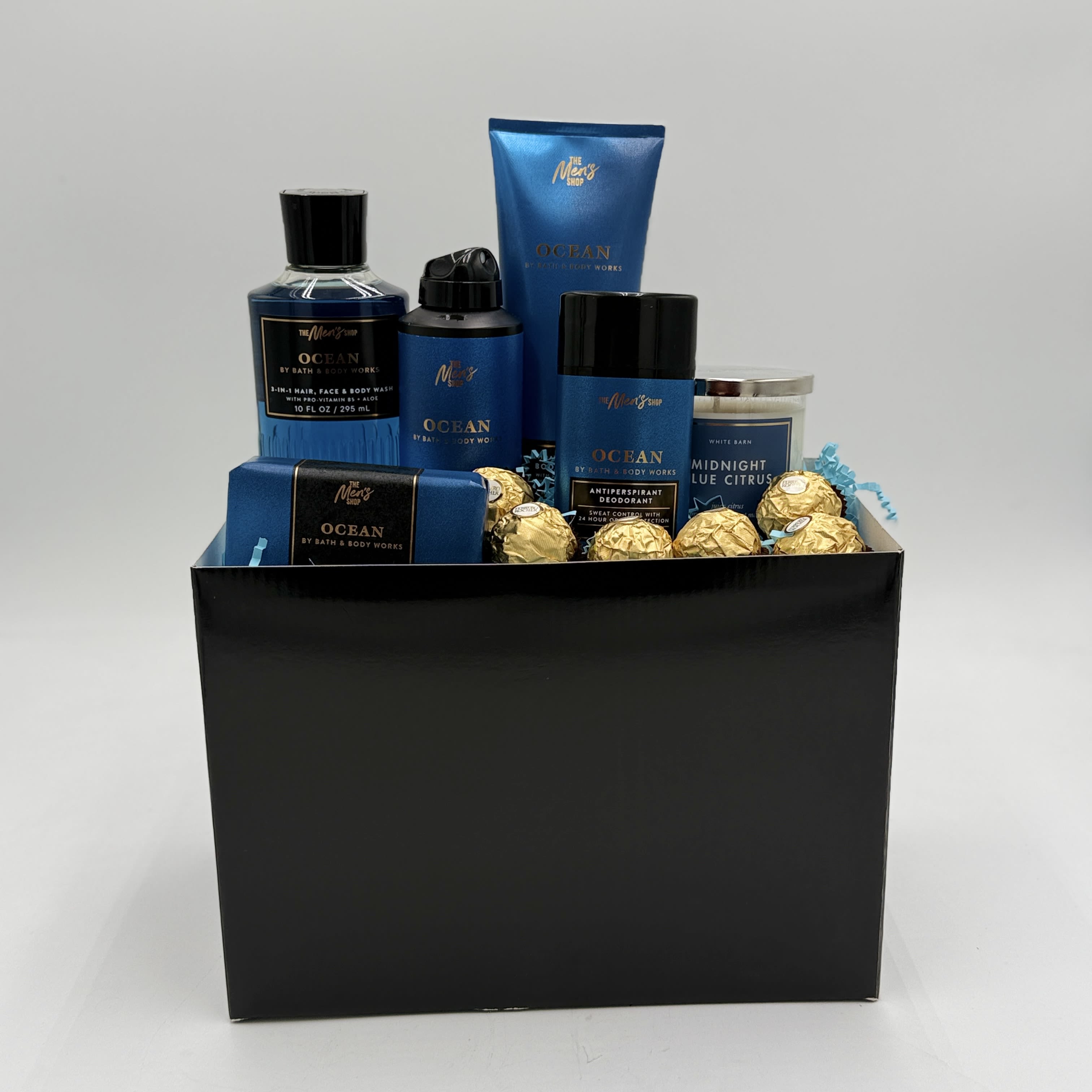 Luxury Men's  Spa Gift Box - Matte black and navy tones give this Luxury Men's Spa Gift Box a polished, masculine look that reads as thoughtfully curated rather than last-minute. Perfect as a birthday gift, Father's Day surprise, or a thank-you present, this spa gift box sends a clear message of care and relaxation-the kind of box that makes the man you're thinking of feel noticed and appreciated.  Arranged in a large matte black gift box, the set includes a body wash bottle, body lotion tube, deodorant stick, soap bar, and a candle jar, all in a coordinated navy-and-black palette with white labeling and gold-wrapped chocolate truffles adding a luxe metallic accent. The composition is clean and retail-ready, with each grooming item presented so it's ready to gift straight from the box.  Ideal for dads, partners, or colleagues who value practical luxury, this collection balances daily essentials with a small indulgence in chocolate and candlelight for at-home relaxation. Size and exact product specifications match the pictured set-ready to ship in its gift-ready packaging for easy sending and immediate delight.