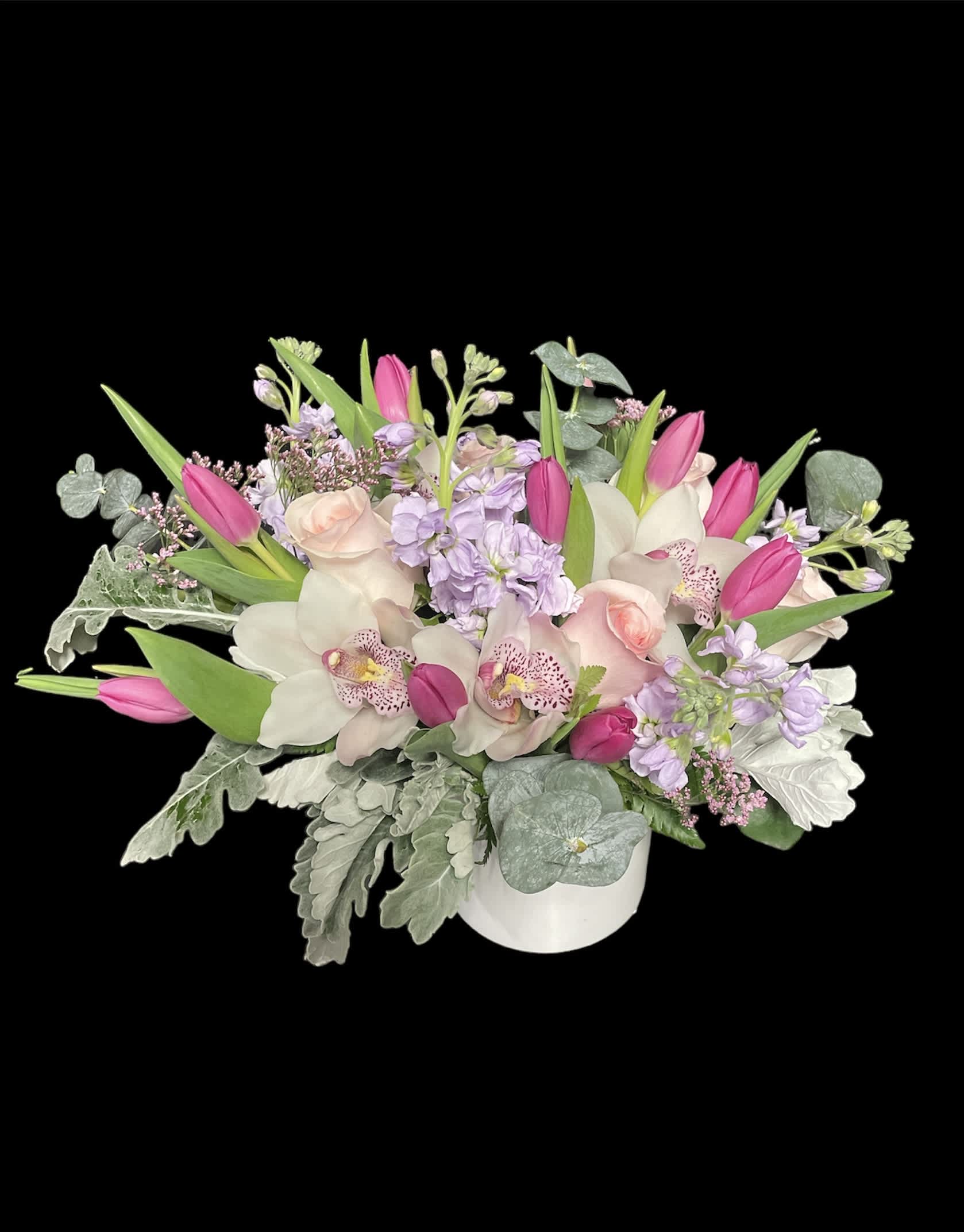 Low pastel arrangement with pink tulips, blush roses, orchids and lavender blooms in a white vase