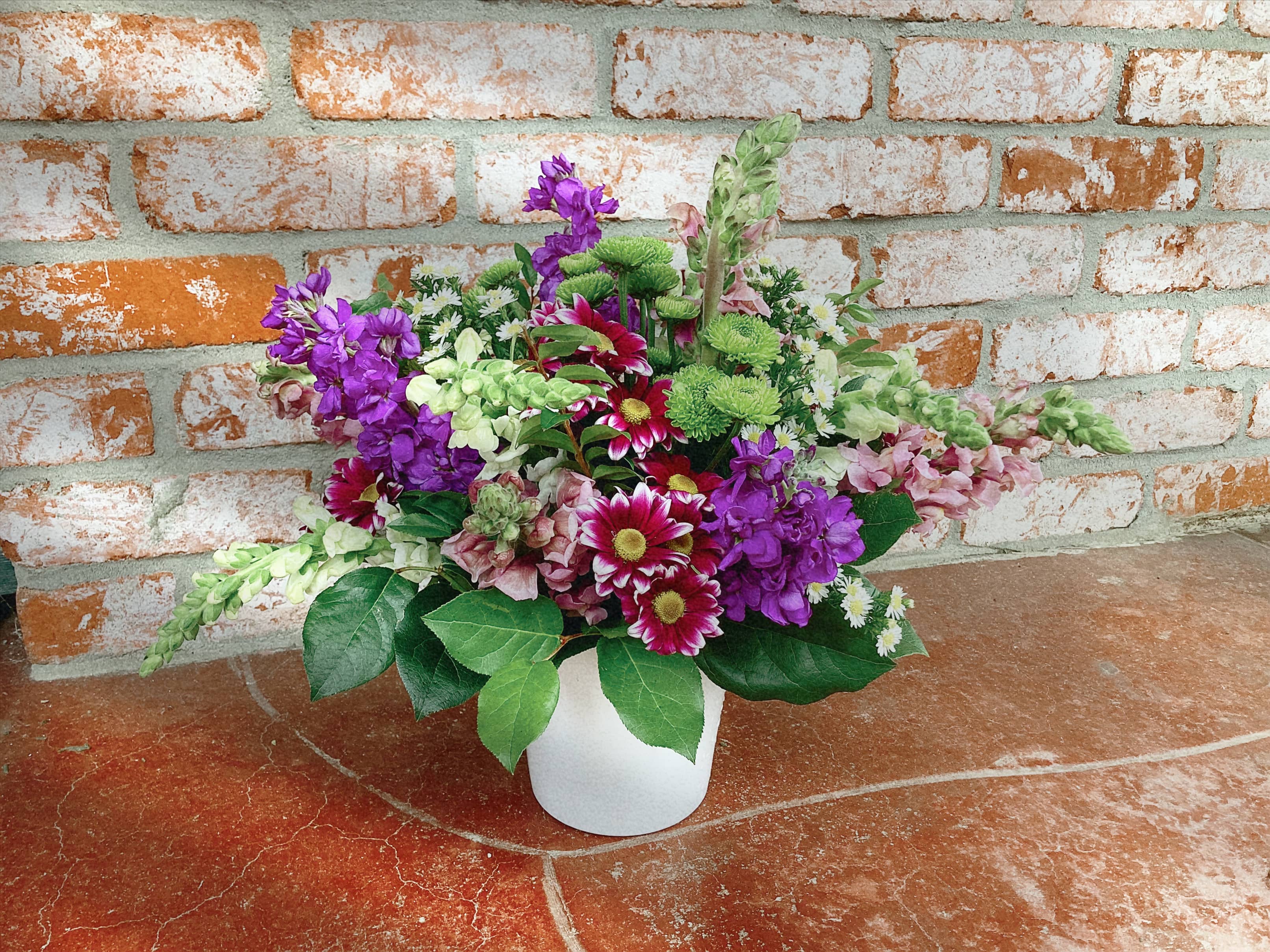 Mixed bouquet of purple, pink, white, and green flowers in a white vase