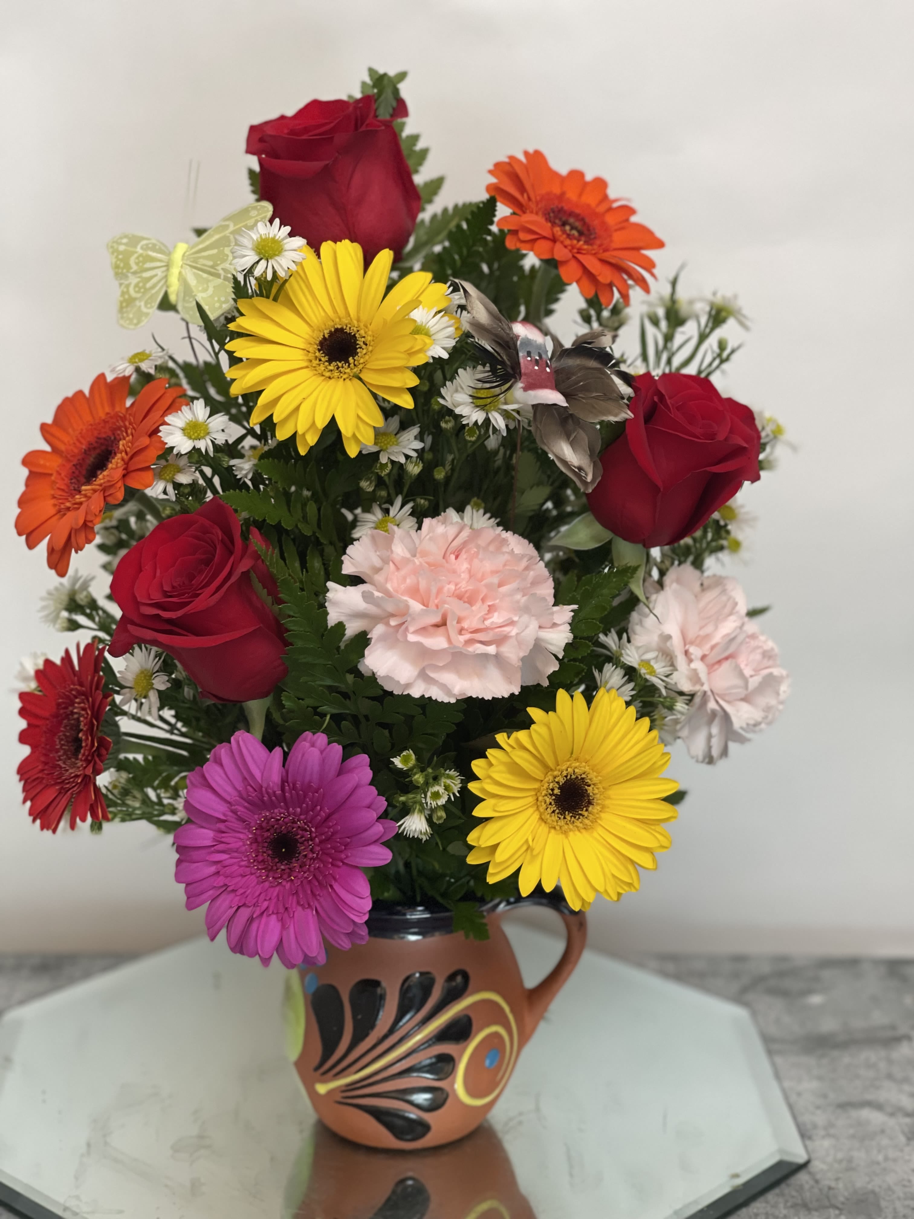 Mixed bouquet of roses, gerbera daisies, and carnations in a decorative mug