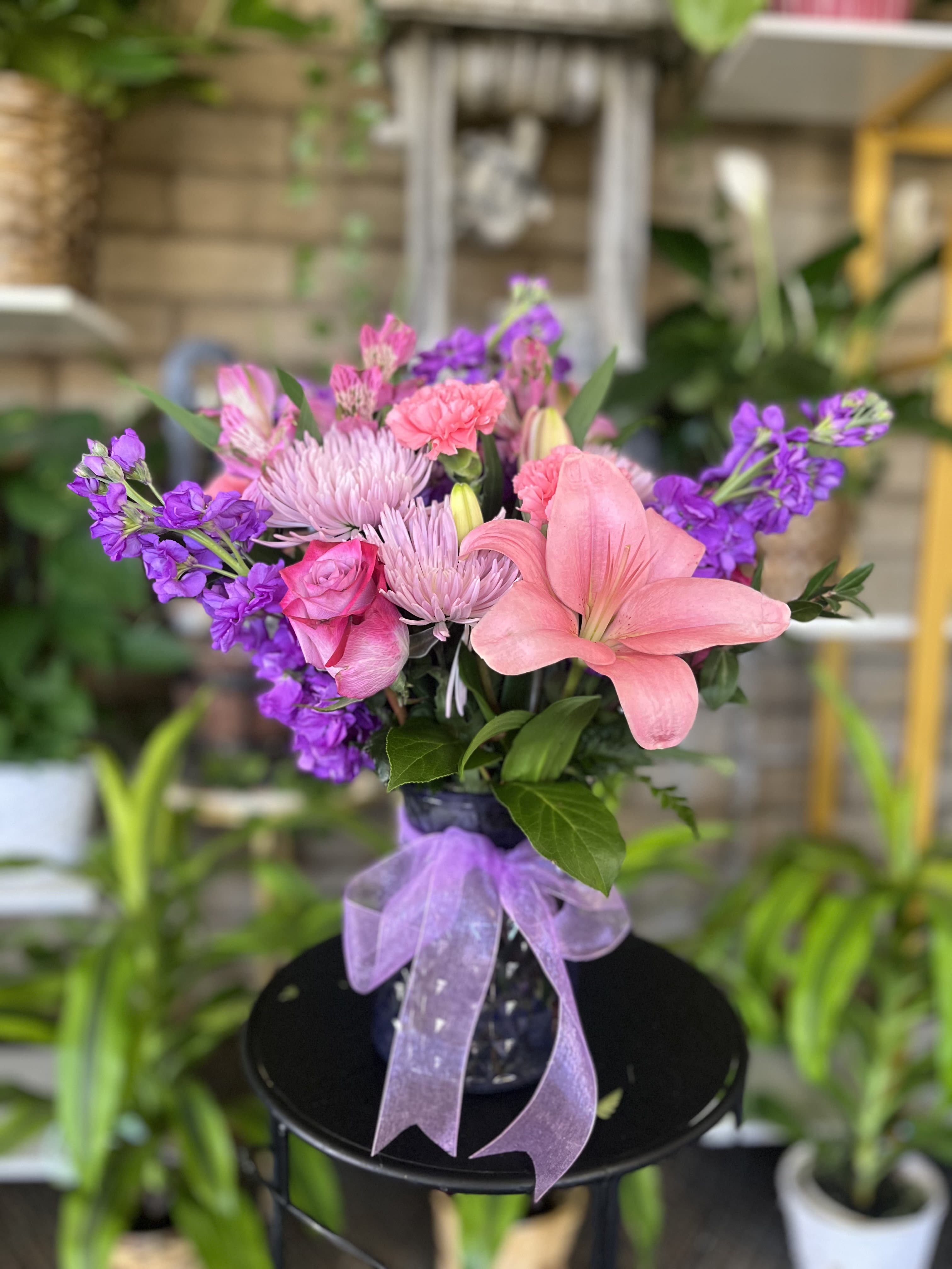 Pink and purple mixed bouquet in a dark vase with a lavender ribbon