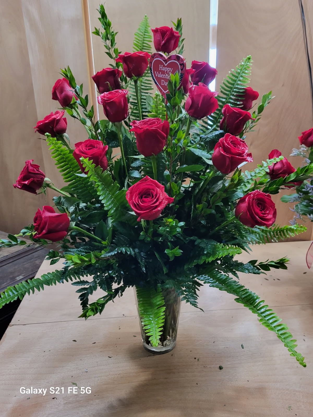 Tall bouquet of red roses in a clear glass vase with fern foliage