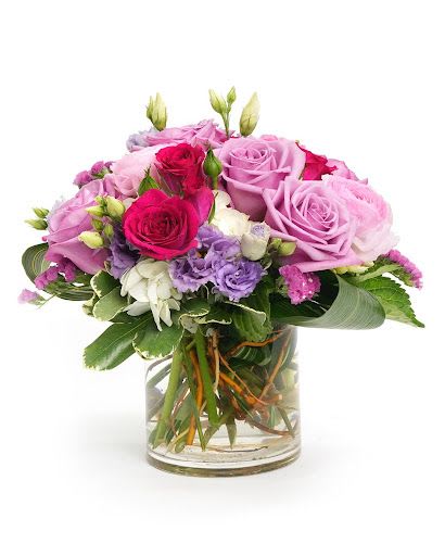 Round arrangement of pink and purple roses with white and lavender blooms in a clear glass vase