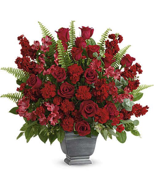 Teleflora's Bold Tribute Bouquet - Bold and beautiful, this majestic mix of red roses and fresh greens in a large, stone-inspired pot is a show of strength and support. Red roses, red alstroemeria, red carnations, miniature red carnations, and burgundy stock are arranged with spiral eucalyptus, seeded eucalyptus, sword fern, and lemon leaf. Delivered in Teleflora's Modern Heritage pot. Orientation: One-Sided