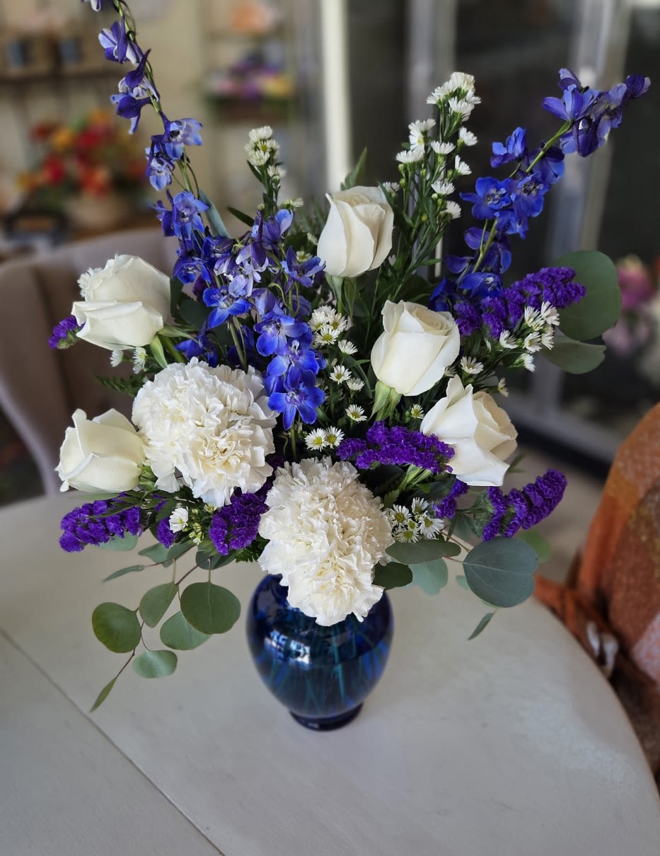 White roses and carnations with blue delphinium in a blue vase