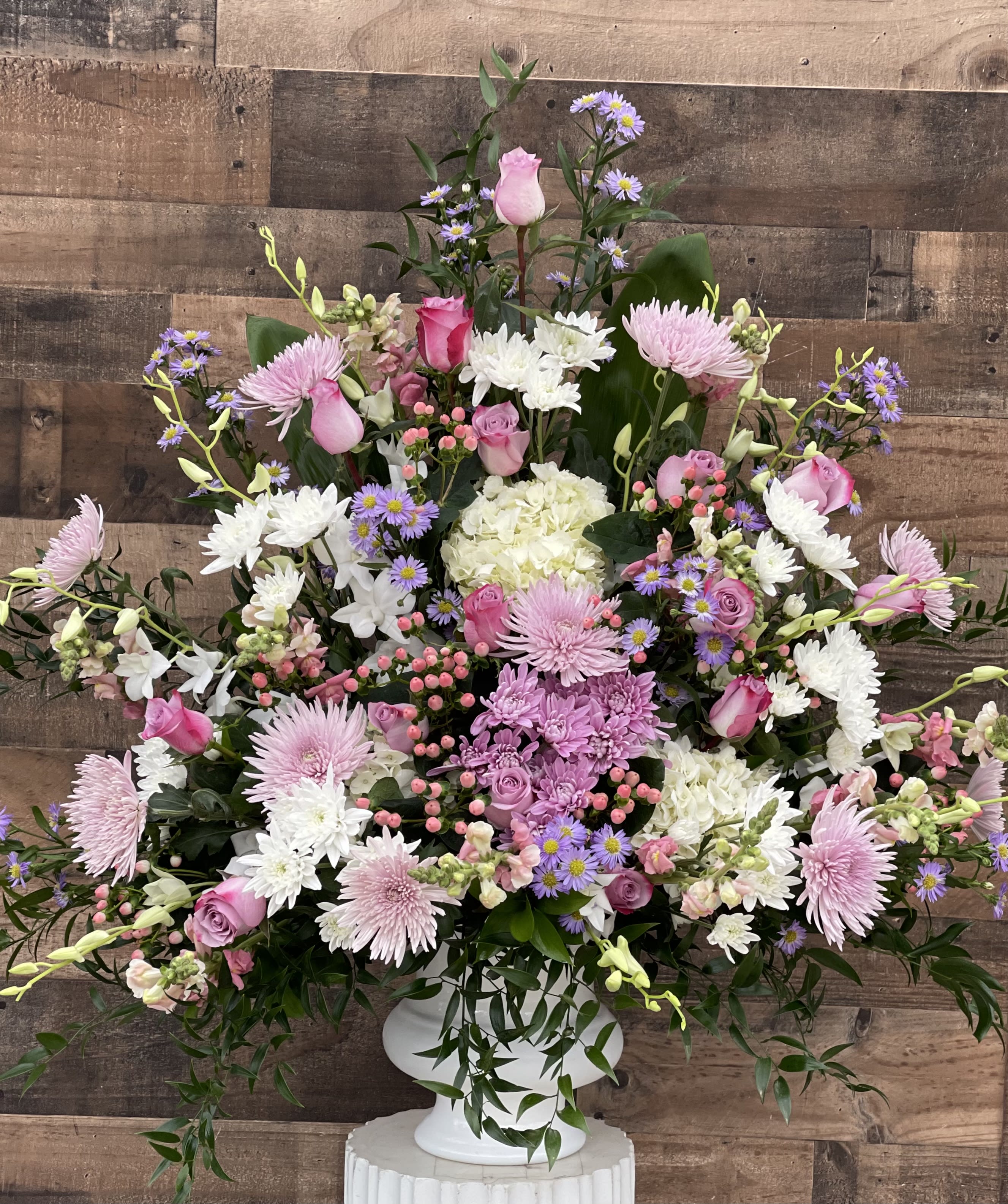 Large pink, white, and lavender floral arrangement in a white pedestal vase.