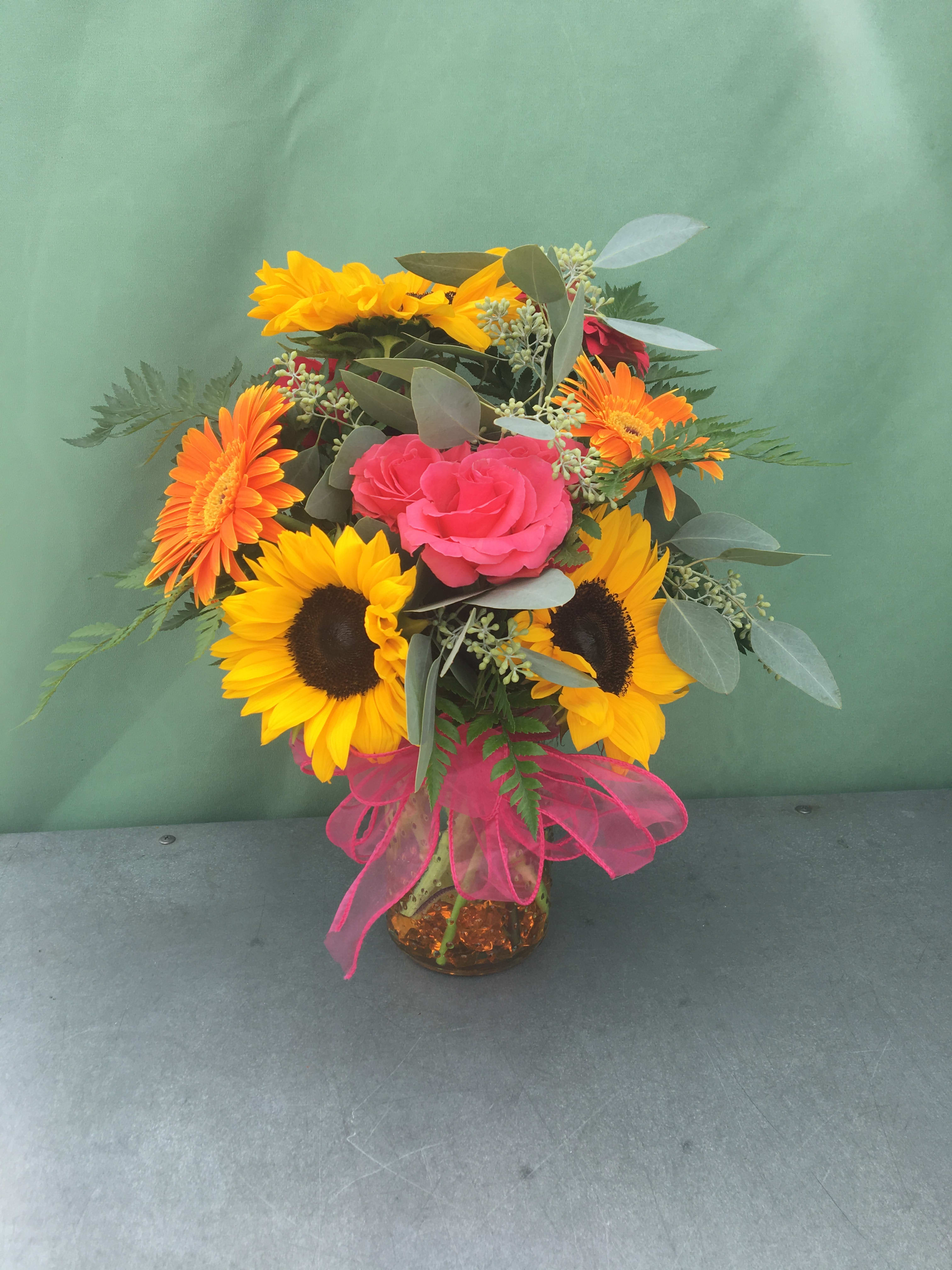 Bouquet of sunflowers, pink roses, and orange gerbera daisies in a glass vase