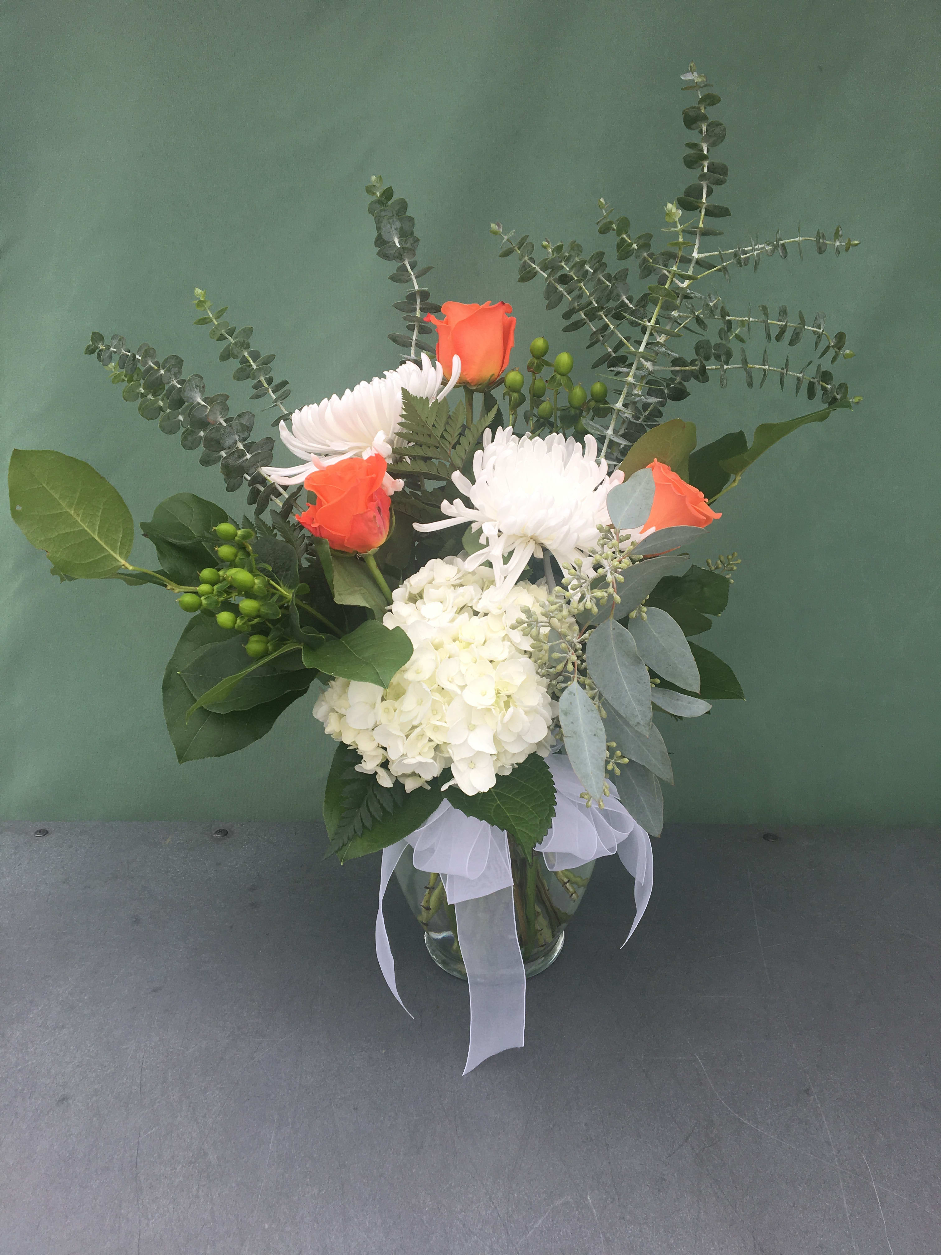 Bouquet of orange roses, white chrysanthemums, and white hydrangea in a glass vase