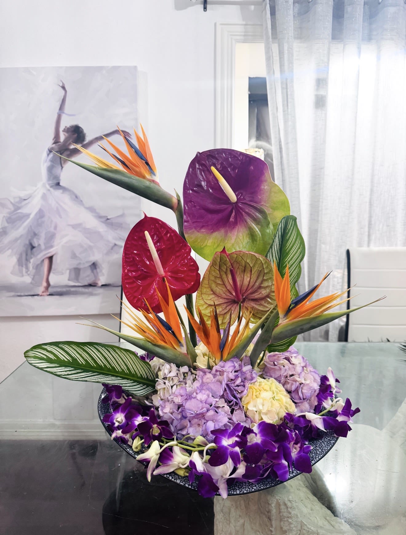 Tropical Flame of Paradise - This arrangement feels like a collision between a rainforest and a luxury fashion editorial. It has a dramatic, sculptural energy. Statement piece designed to dominate a room. Is an ultra-premium tropical floral sculpture designed for those who live boldly and beautifully. Exotic Birds of Paradise rise above rare Anthuriums and cascading orchids, creating a masterpiece of color, texture, and movement.