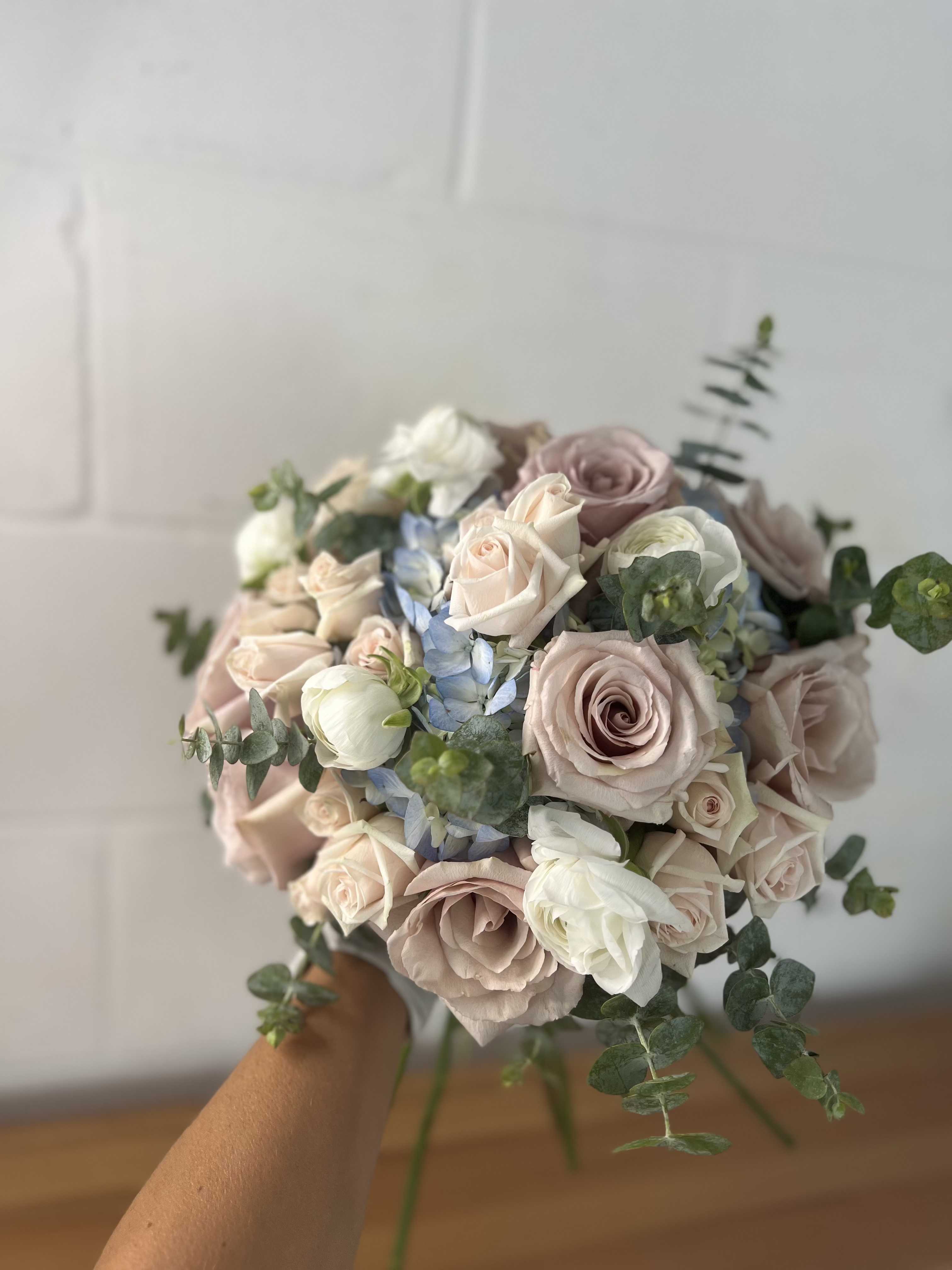 Handheld bouquet of blush roses, white blooms, and blue flowers