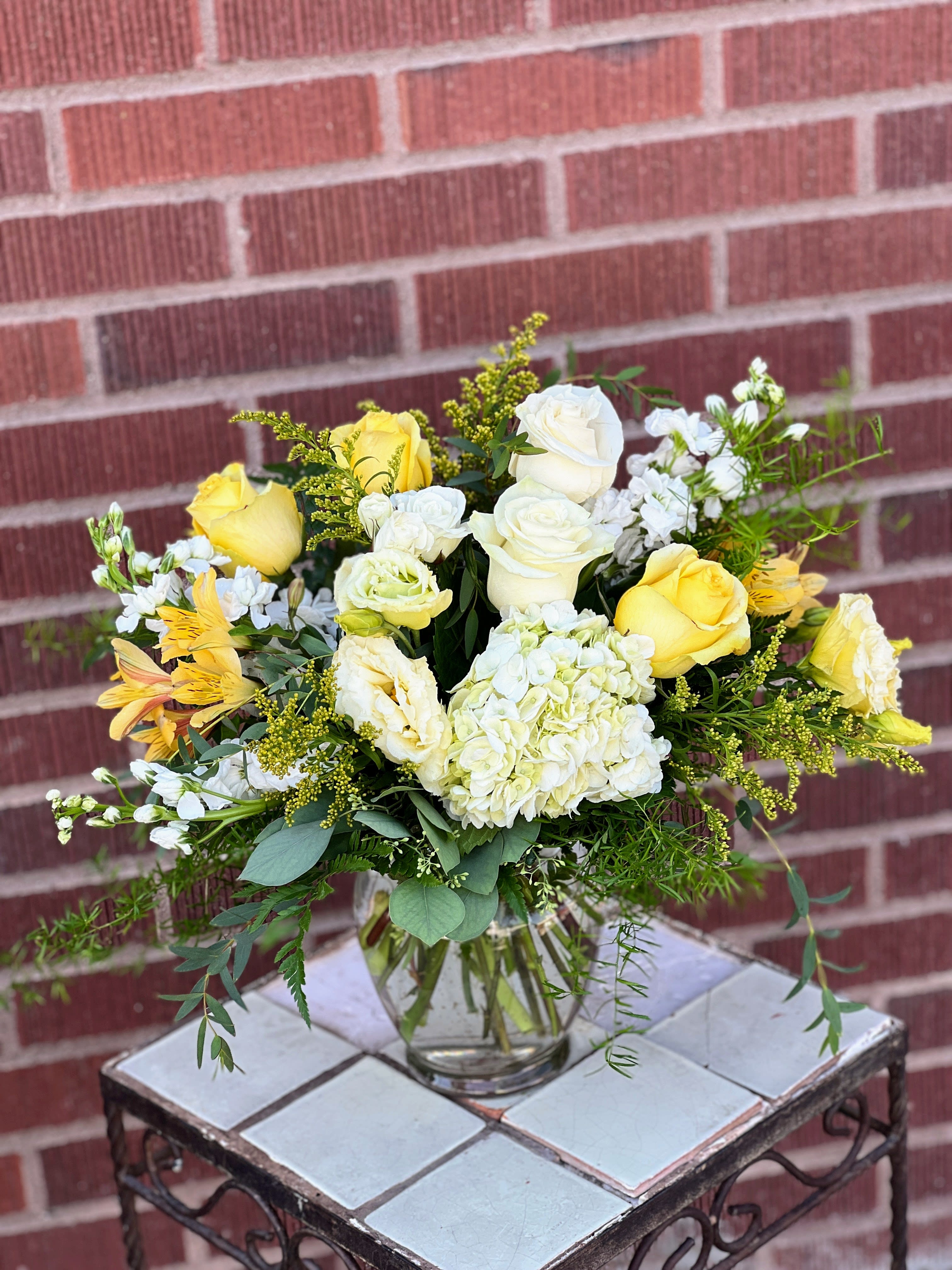 Yellow and white roses in a clear glass vase with mixed greenery
