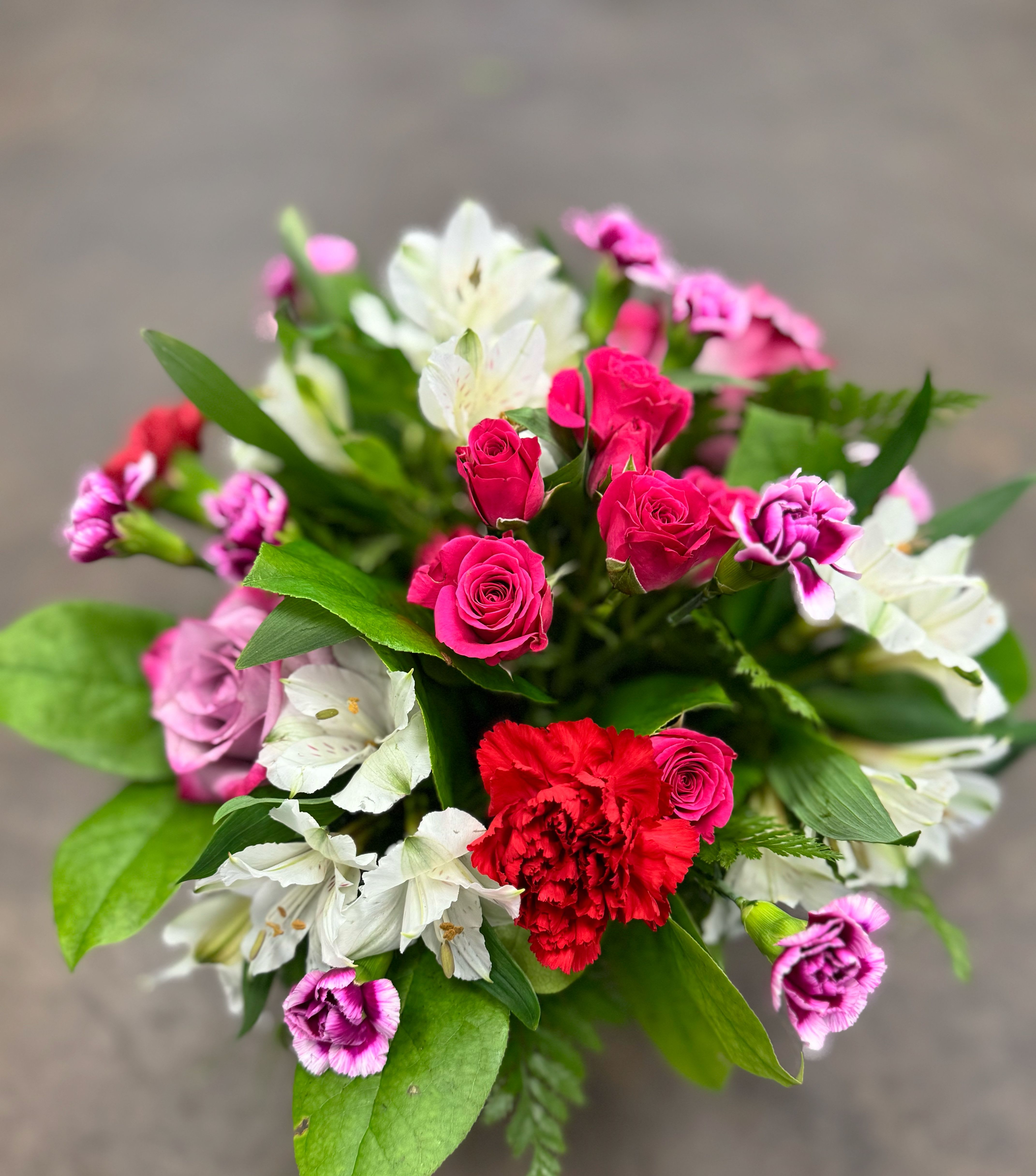 Cherry Lane - A bright and happy mix of mini hot pink spray roses, red and purple carnations, soft lavender roses, and creamy white alstroemeria. Designed in a clear vase with fresh greenery, this cheerful arrangement is full of color and charm. A great pick for birthdays, thank-yous, celebrations, or just because.