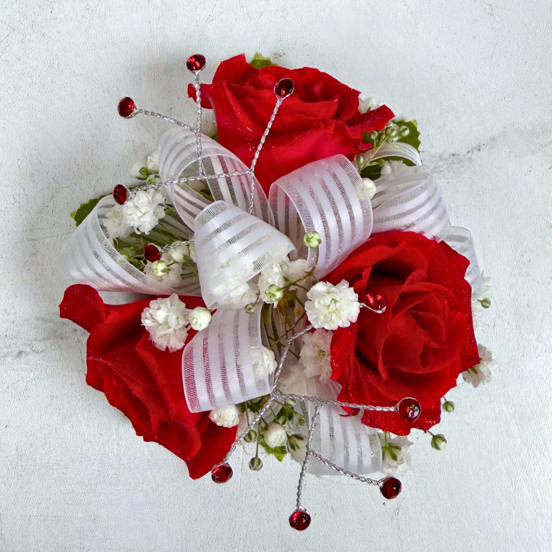 Garnet 3 Rose Wrist Corsage - 3 petite, classy red spray roses form a delicate, wearable cluster in this Garnet 3 Rose Corsage, perfect for prom. The deep red, white and green palette reads refined and sophisticated, the kind of piece that makes the wearer feel like a movie star on their big night.  The corsage pairs three small, compact red roses with fluffy baby's breath filler, finished with a semi sheer white bow and small red rhinestone gems for a touch of sparkle. Hand-assembled to sit comfortably on the wrist with a white lace wristlet, it's small, neatly constructed, and designed to coordinate with formalwear and pastel palettes. Light misting and keeping it cool until wear helps maintain bloom freshness.