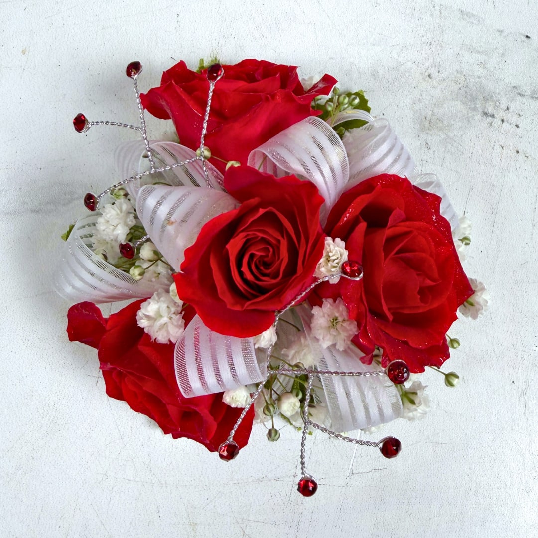 Garnet 4 Rose Corsage - 4 petite, classy red spray roses form a delicate, wearable cluster in this Garnet 4 Rose Corsage, perfect for prom. The deep red, white and green palette reads refined and sophisticated, the kind of piece that makes the wearer feel like a movie star on their big night.  The corsage pairs four small, compact red roses with fluffy baby's breath filler, finished with a semi sheer white bow and small red rhinestone gems for a touch of sparkle. Hand-assembled to sit comfortably on the wrist with a white lace wristlet, it's small, neatly constructed, and designed to coordinate with formalwear and pastel palettes. Light misting and keeping it cool until wear helps maintain bloom freshness.