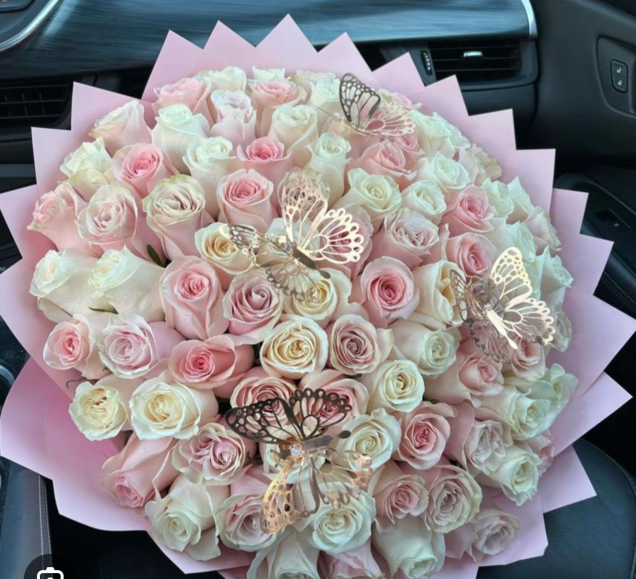 100 Roses pink and white with decorations - A lavish dome of 100 roses in pale pink and creamy white makes an unforgettable anniversary bouquet or wedding gift that reads as pure romance. This flower arrangement for anniversaries, birthdays, or special celebrations places the recipient front and center-she'll feel cherished and adored the moment the butterflies and ribbon catch her eye.  Tightly packed roses create a plush, full silhouette wrapped in soft pink paper for a refined, feminine presentation. Decorative metallic butterfly picks and a coordinating ribbon add whimsical shine and motion against the velvety rose petals, while the neutral-pink palette keeps the look timeless and elegant.  Perfect for marking milestones, saying "I love you," or making a big birthday impression, this arrangement arrives ready to display; trim the stems and change the water every other day to keep blooms fresh longer. For a show-stopping floral statement that feels both romantic and celebratory, this bouquet makes the moment truly special.
