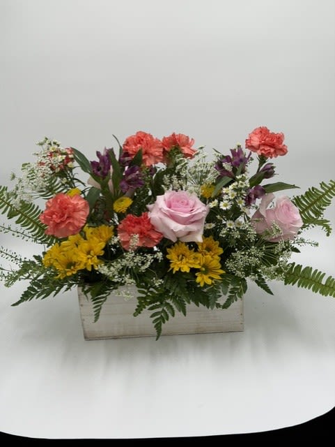 Garden Party Charm - This cheerful arrangement features soft pink roses, coral carnations, sunny yellow daisies, and delicate seasonal accents in a rustic wooden container. The mix of textures and bright garden-inspired blooms creates a fresh, welcoming feel. Perfect for birthdays, thank-you gifts, or simply adding a little happiness to someone’s day.
