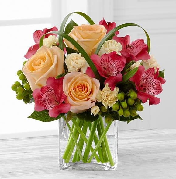 The All Aglow™ Bouquet by Better Homes and Gardens® - We proudly present the Better Homes and Gardens® All Aglow™ Bouquet. Light up their life with incredible color and blooming beauty when you send this exquisite flower bouquet. Unforgettable peach roses are surrounded by red Peruvian lilies, pale yellow mini carnations, green hypericum berries, lily grass blades, and lush greens to create a stunning flower arrangement. Presented in a clear glass cube vase to give it a sophisticated look, this mixed flower bouquet will express your sweetest thank you, get well, or congratulations wishes.