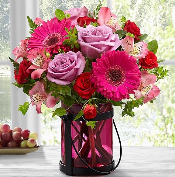 The Pink Exuberance Bouquet by Better Homes and Gardens® - We proudly present the Better Homes and Gardens® Pink Exuberance™ Bouquet. Boldly blushing with an array of pink hues and offering an unforgettable styling your special recipient will adore, this mixed flower bouquet is set to send sweet wishes with gorgeous grace. Lavender roses, hot pink Peruvian Lilies, fuchsia gerbera daisies, red spray roses and lush greens are brought together to create a perfectly pink presentation. Arranged in a pink glass lantern inspired vase that can be used as a candle holder after the original offering of flowers fades, this mixed flower bouquet will make an excellent birthday, thank you, or congratulations gift.