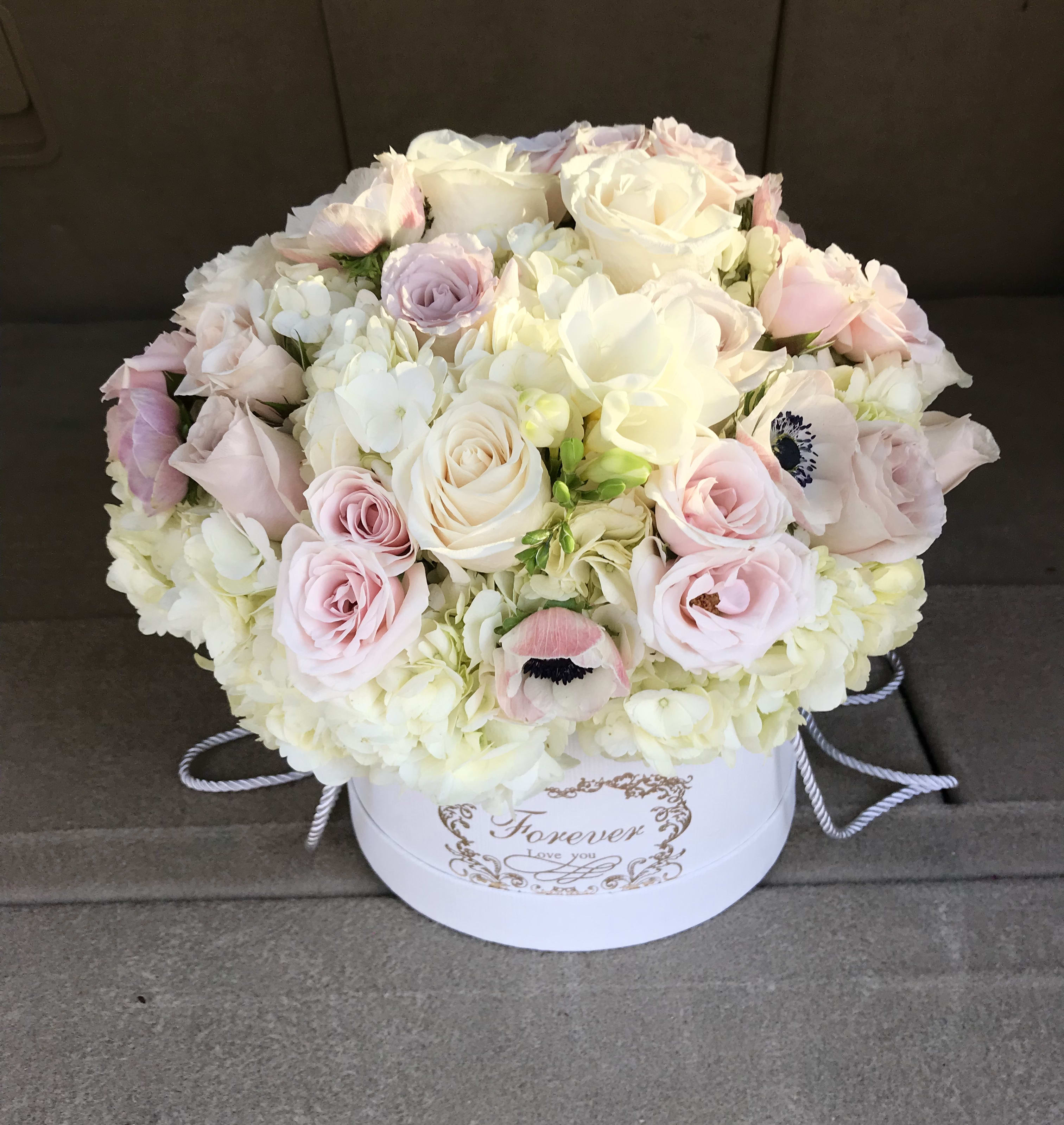 Round bouquet of pale pink and white roses in a white hatbox