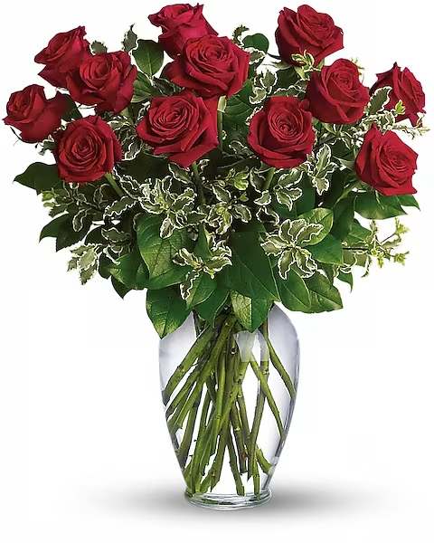 Red roses arranged in a clear glass vase with variegated greenery
