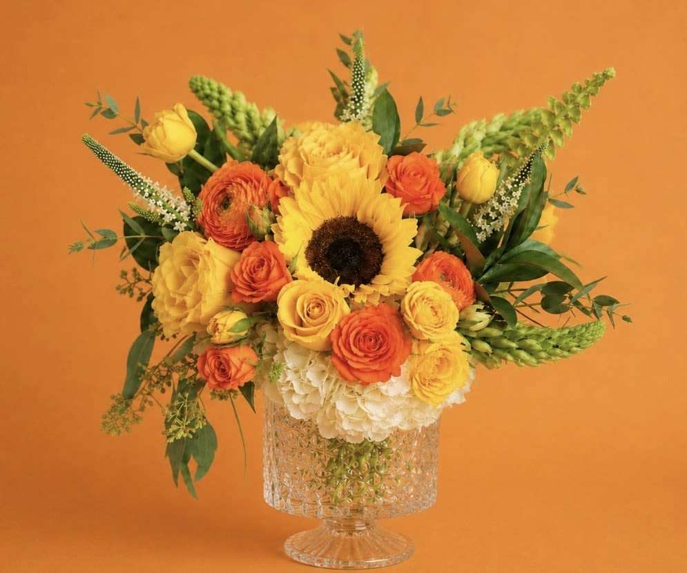 Golden Sunshine Garden – Mother’s Day Flowers | DFW Florist - Bright, happy, and full of life—our Golden Sunshine Garden is designed for the mom who loves cheerful yellows, warm oranges, and sunny vibes.  Inspired by the arrangement shown, this design features a radiant color palette and a lush, rounded shape that makes a statement. A sunflower or similar focal bloom may be included when available to enhance the sunny feel.  As always, we use premium, fresh flowers and design each arrangement to match the color palette, size, and overall style, while allowing for natural variation based on seasonal availability.   Best for: Yellow, orange, and bright color lovers  Style: Bold, cheerful, and eye-catching  Delivery: Same-day options available in DFW