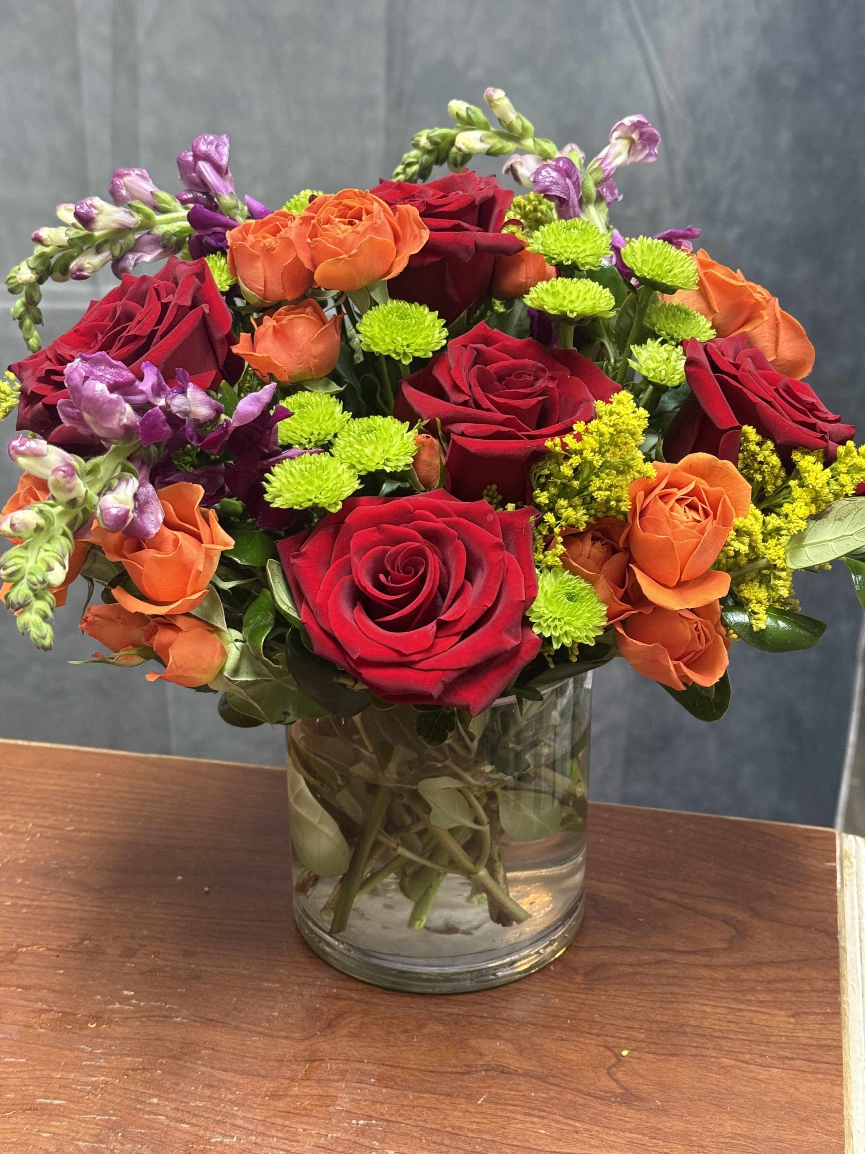 Mixed bouquet of red, orange, and purple flowers in a glass vase