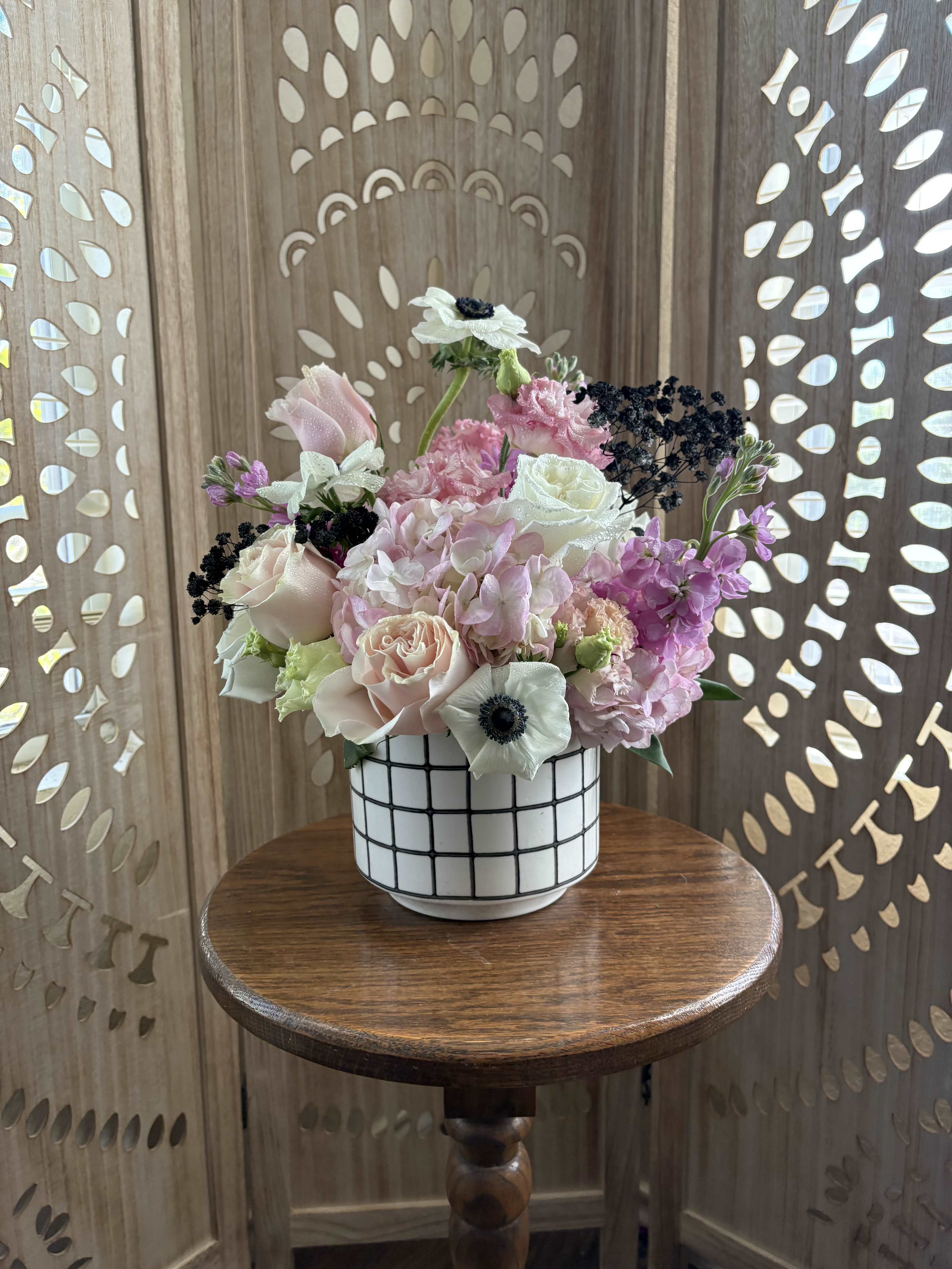 Love Bites - For the lovers of dark romance, loud music, checkered floors, and beauty that doesn’t play by the rules. Designed with moody black baby’s breath and pink, black, and white blooms in a bold checkered ceramic vase, this arrangement is sweet, rebellious, and a little emotionally unavailable.
