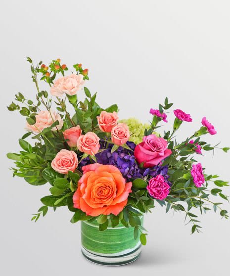 Sunset Garden Charm - delightful garden-style arrangement featuring peach roses, lavender blooms, vibrant pink carnations, and lush greenery artfully designed in a modern glass vase. This fresh and whimsical bouquet brings warmth, happiness, and elegance, making it perfect for birthdays, thank you gifts, celebrations, or simply brightening someone’s day.
