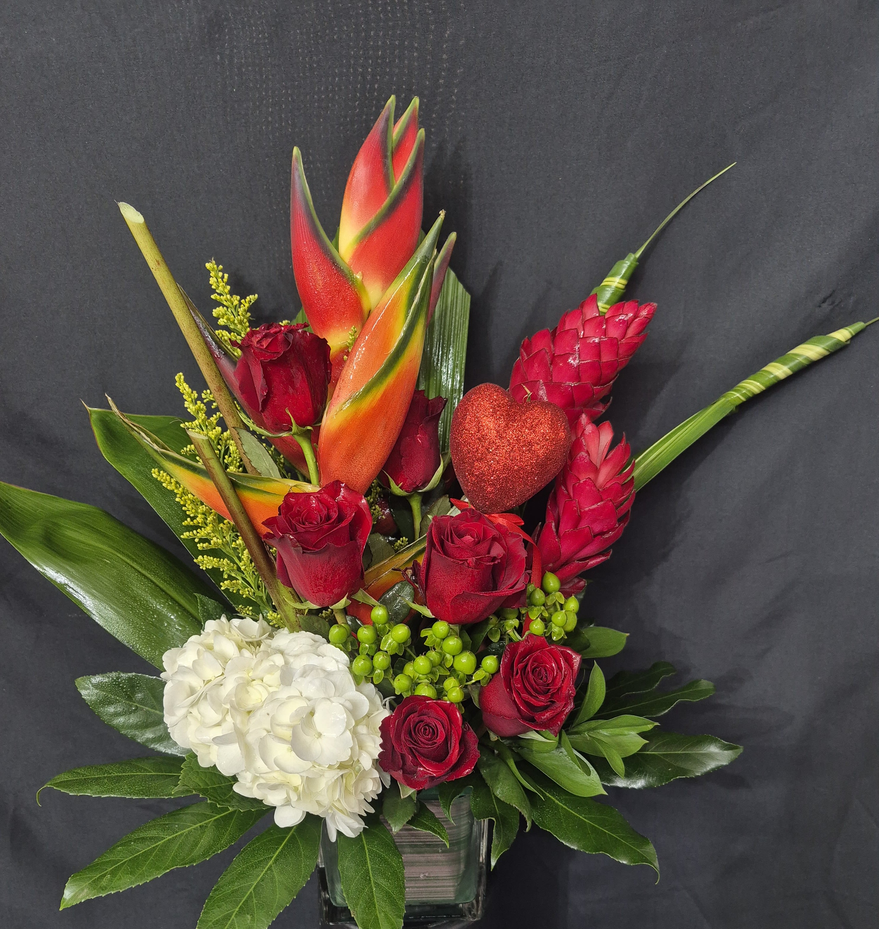 Red roses and white hydrangea in a glass vase with tropical blooms and a glitter heart