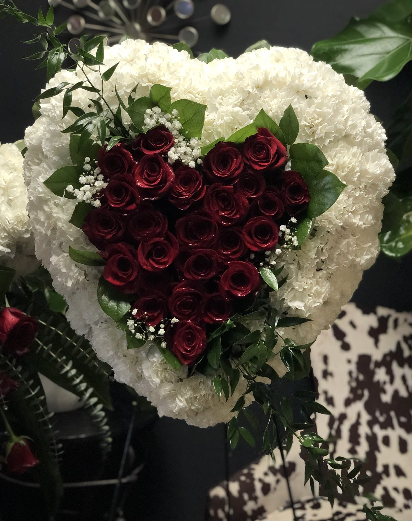 Heart-shaped bouquet of red roses framed by white flowers and greenery