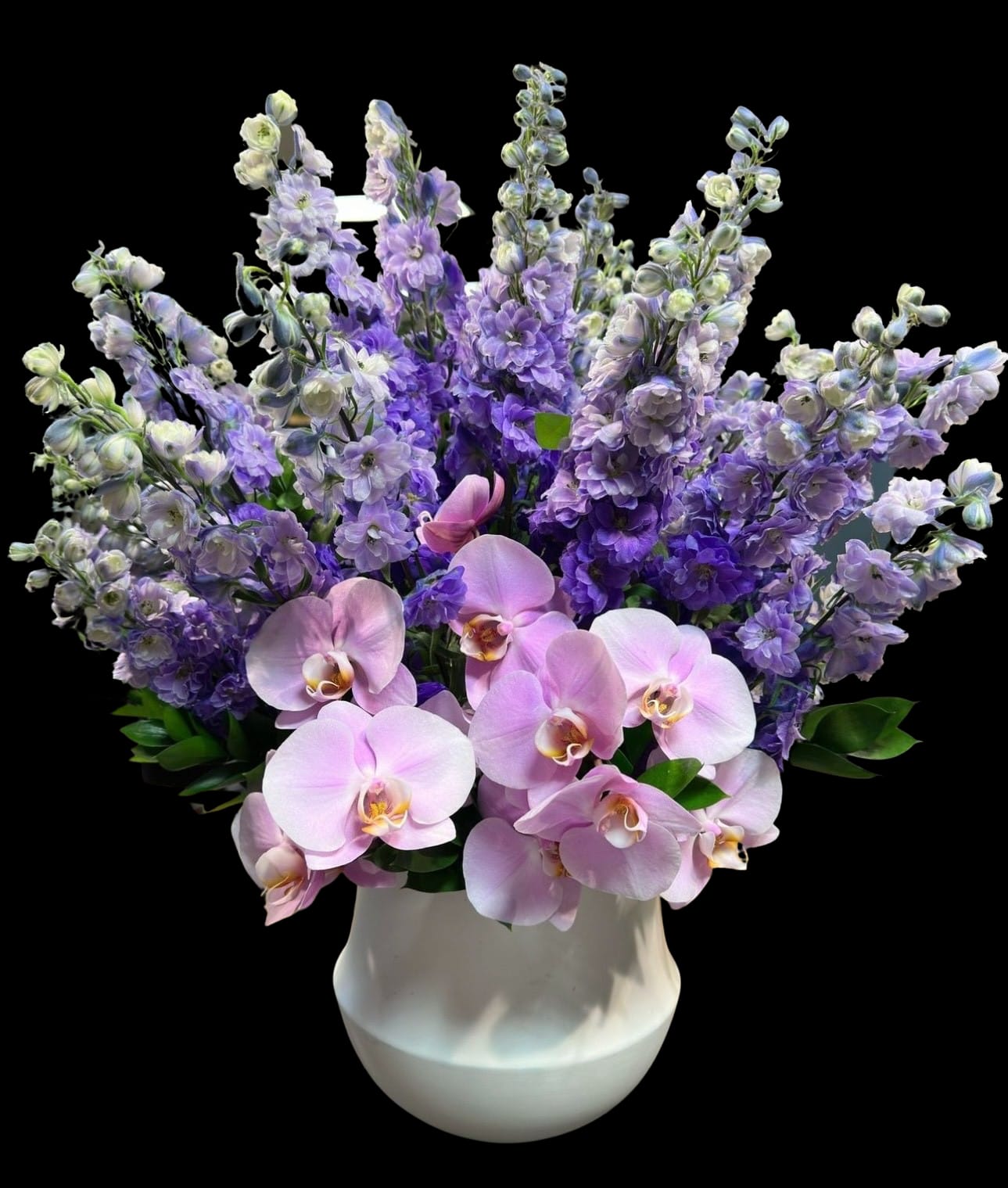 Pink orchids and purple flowers arranged in a white vase