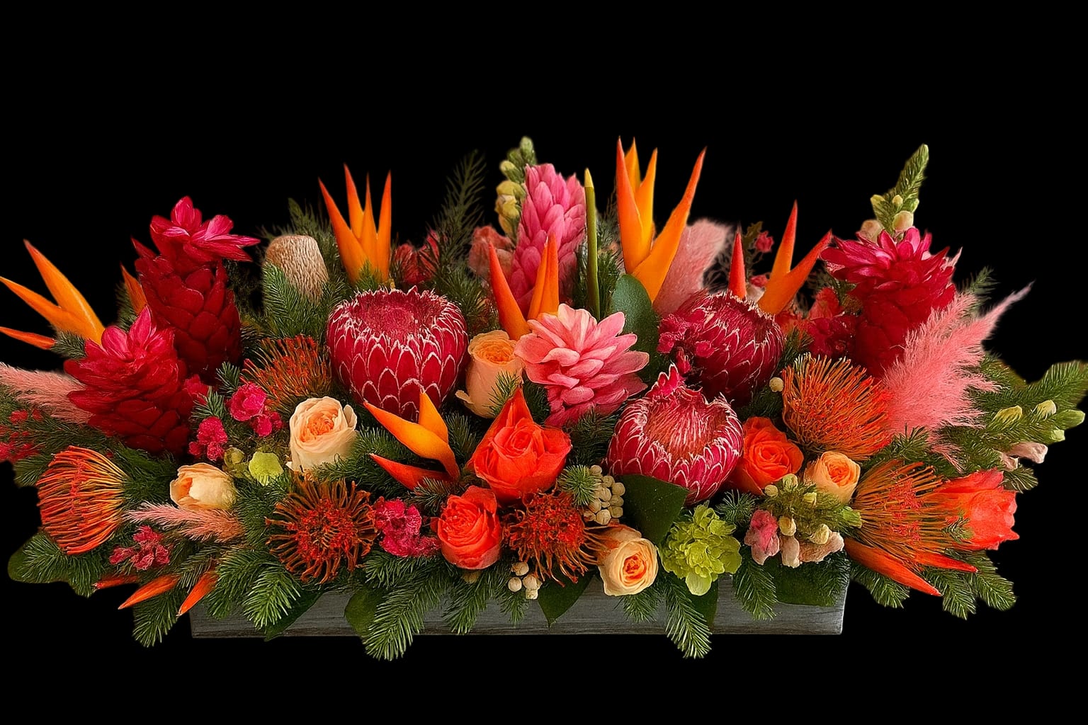 Bright tropical floral arrangement with red, orange, and pink blooms in a low rectangular container