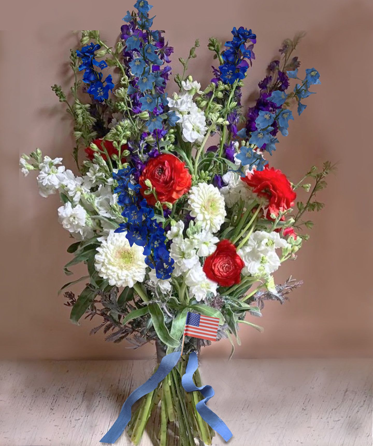 Red White &amp; Blue bouquet - Red, White and Blues in a pretty and symbolic hand tied bouquet of seasonal flowers with a very natural and wild look like blue delphinium, white poppies/cosmos, red ranunculus and peonies. A small American flag is attached.   We offer a personal hand delivery by our own delivery staff and guarantee the flowers will look perfect, when they arrive. 