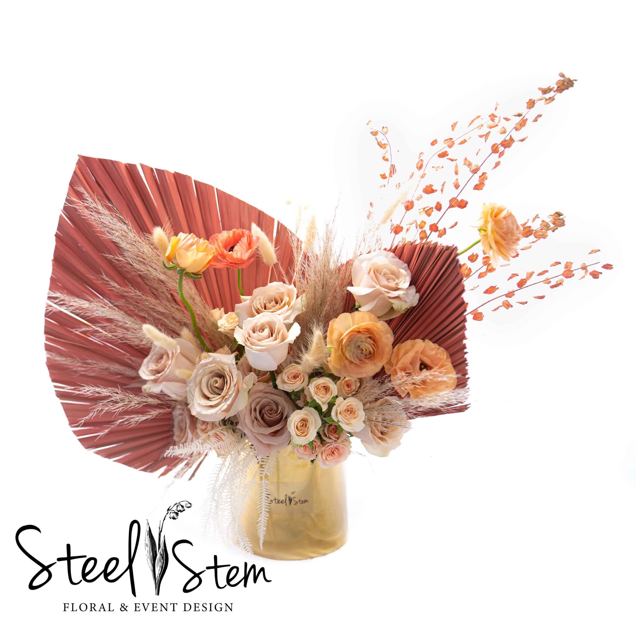 Bouquet of blush and peach roses in a gold vase with fan-shaped dried accents