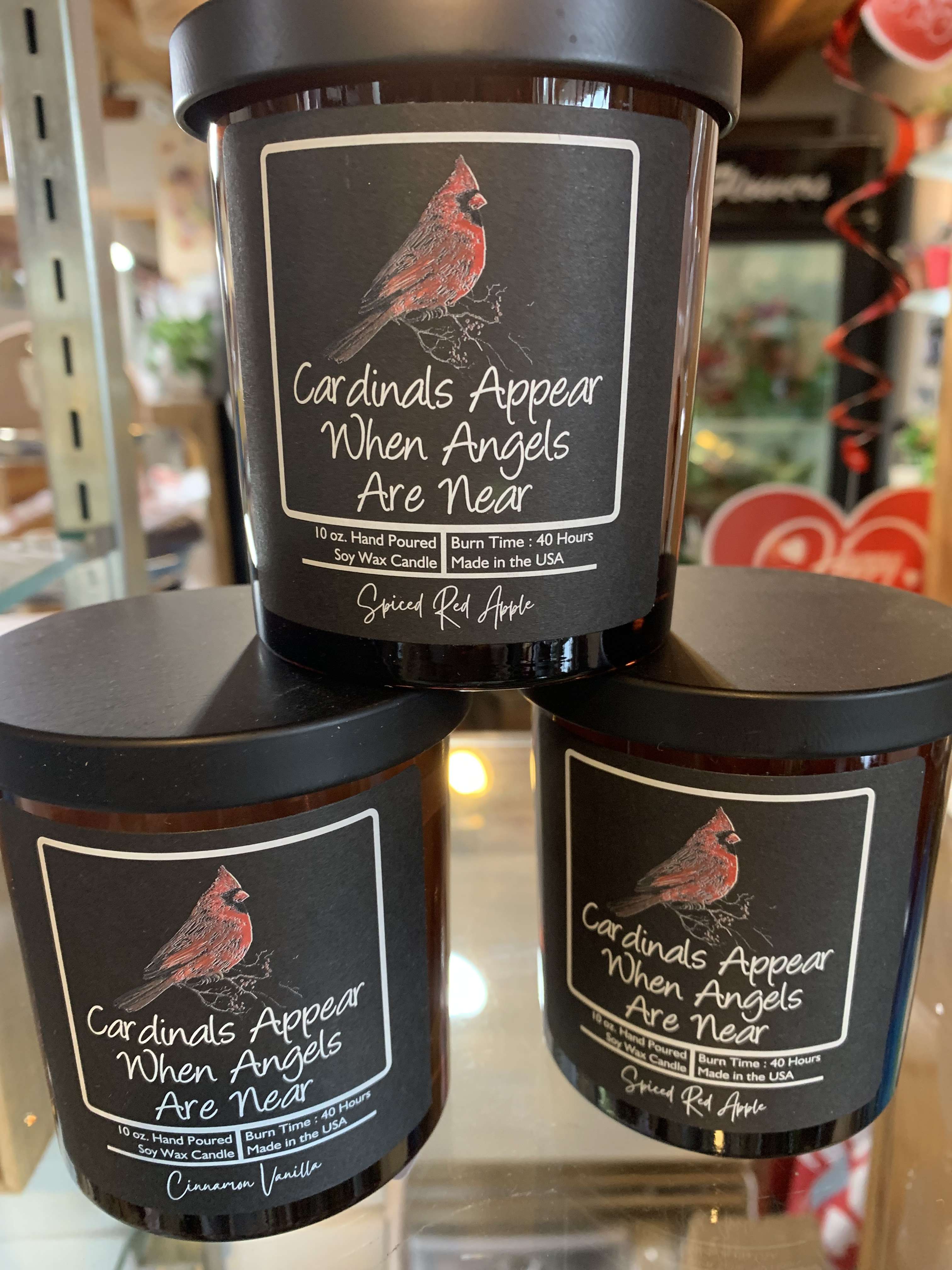 Three black-lidded candles with cardinal labels and memorial text