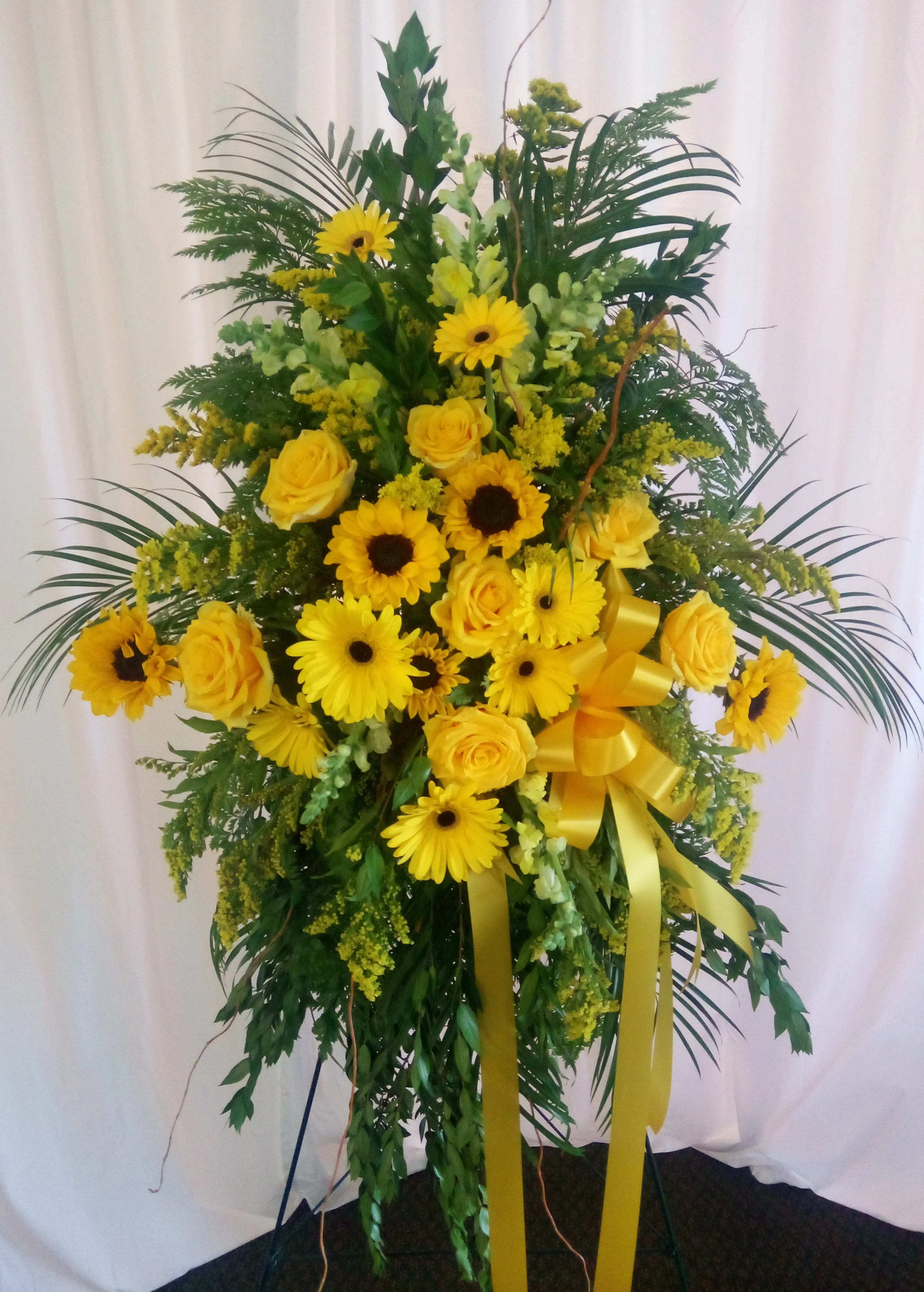 Tall yellow floral spray with roses and daisy blooms on a stand