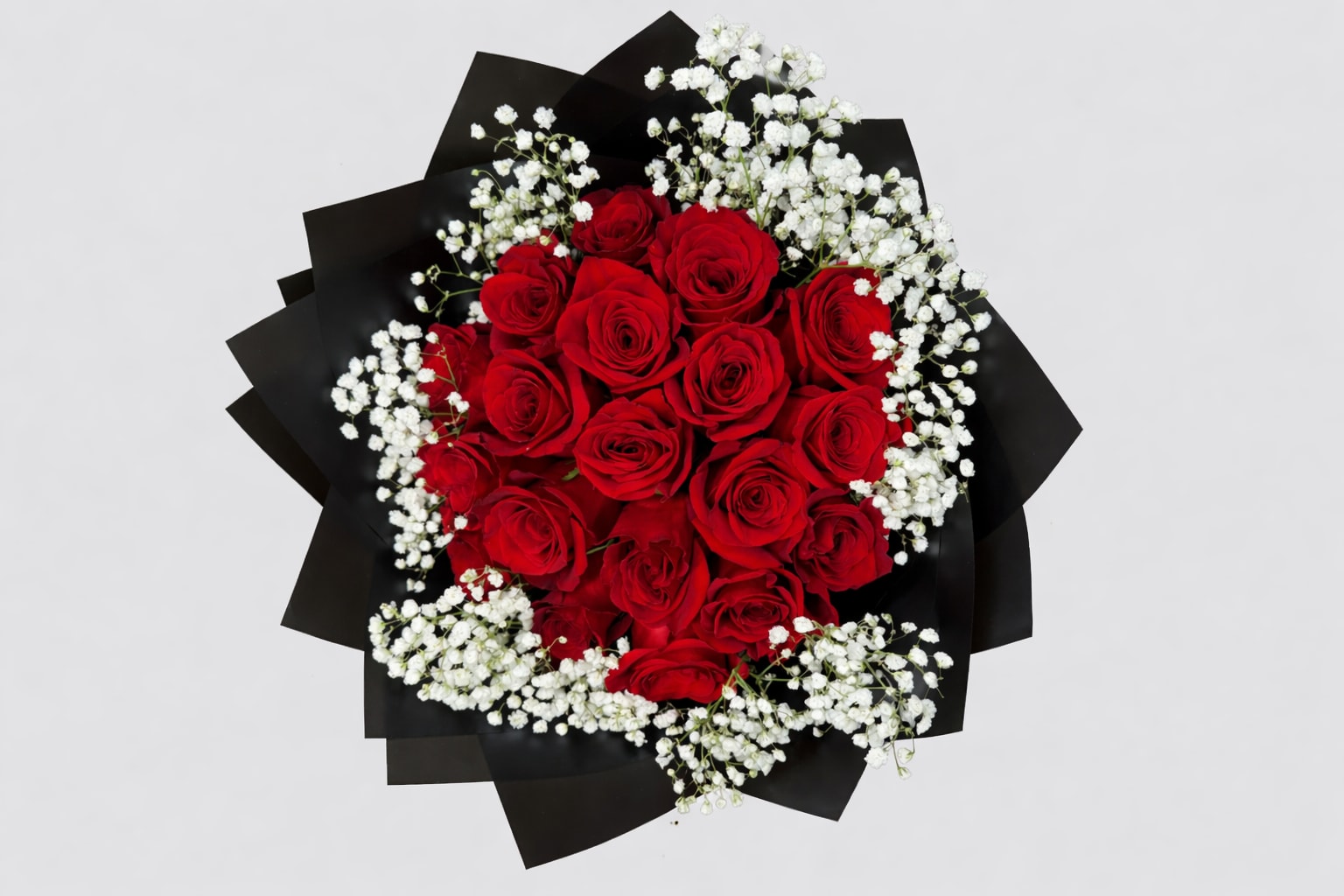 Round bouquet of red roses and white filler flowers wrapped in black paper.